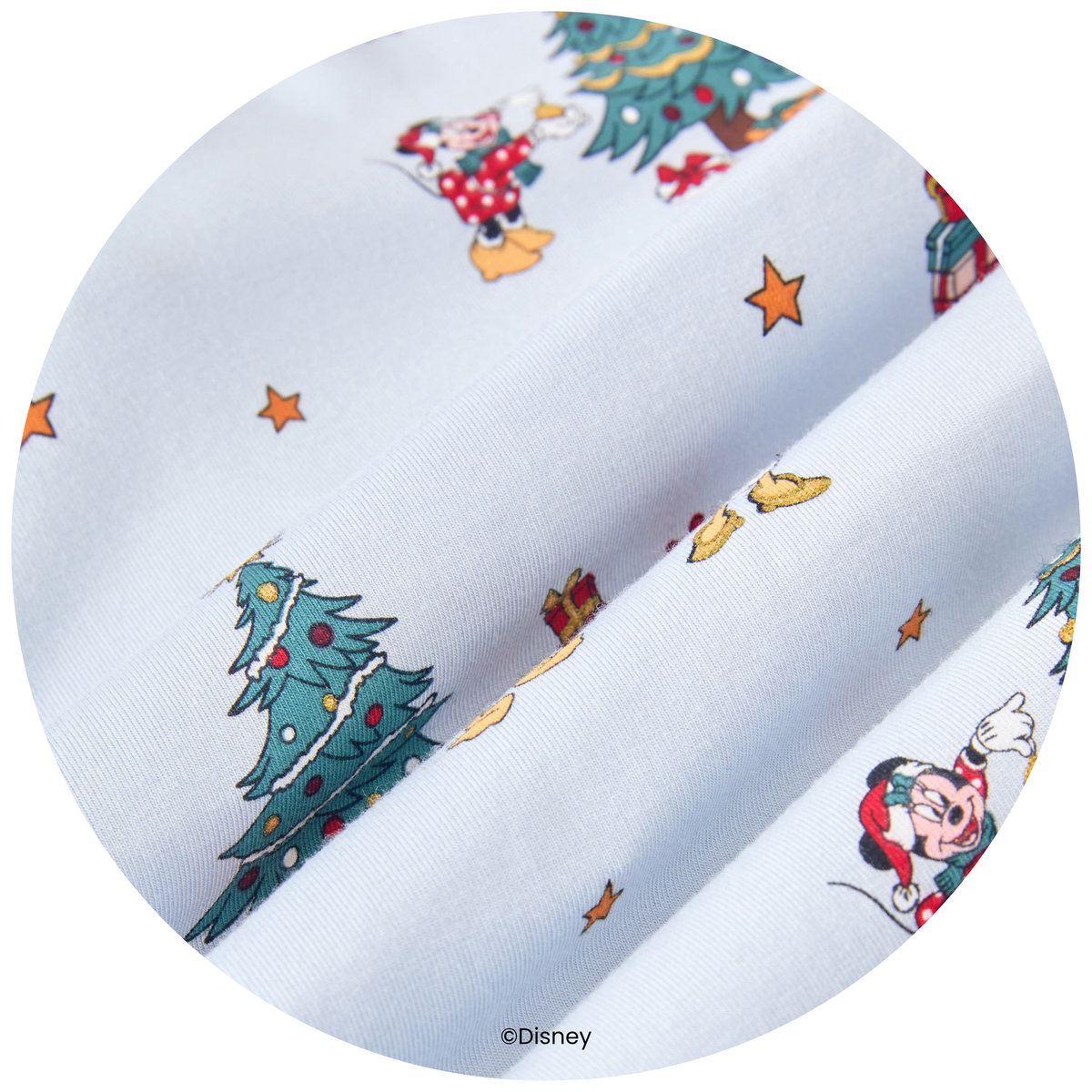 A circular close-up of a light blue fabric with a festive Christmas print featuring Mickey Mouse, Minnie Mouse, Christmas trees, stars, and gifts. A Disney copyright mark is visible at the bottom.