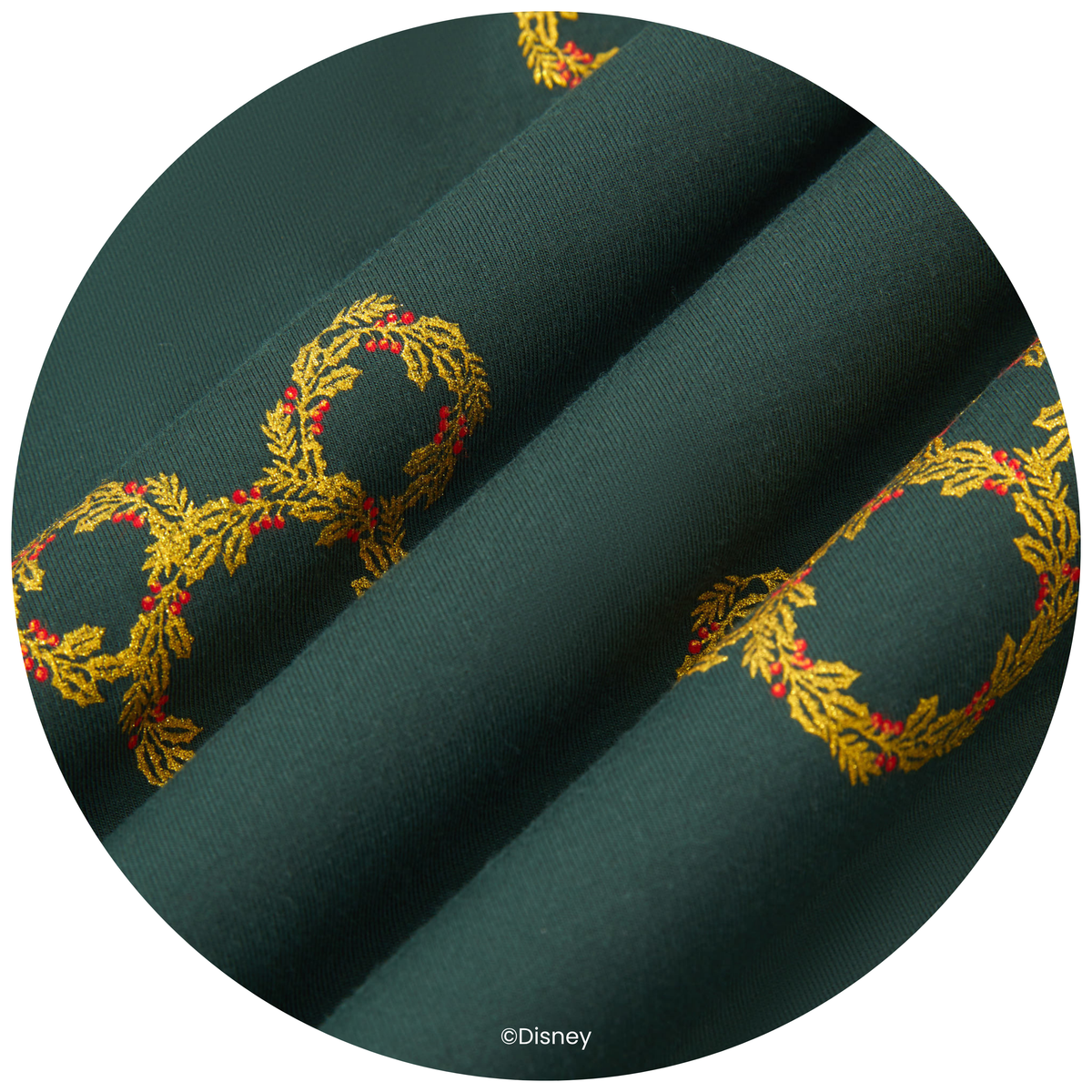 A close-up circular view of dark green fabric with embroidered gold wreaths and small red berry accents. A small Disney watermark appears near the bottom.