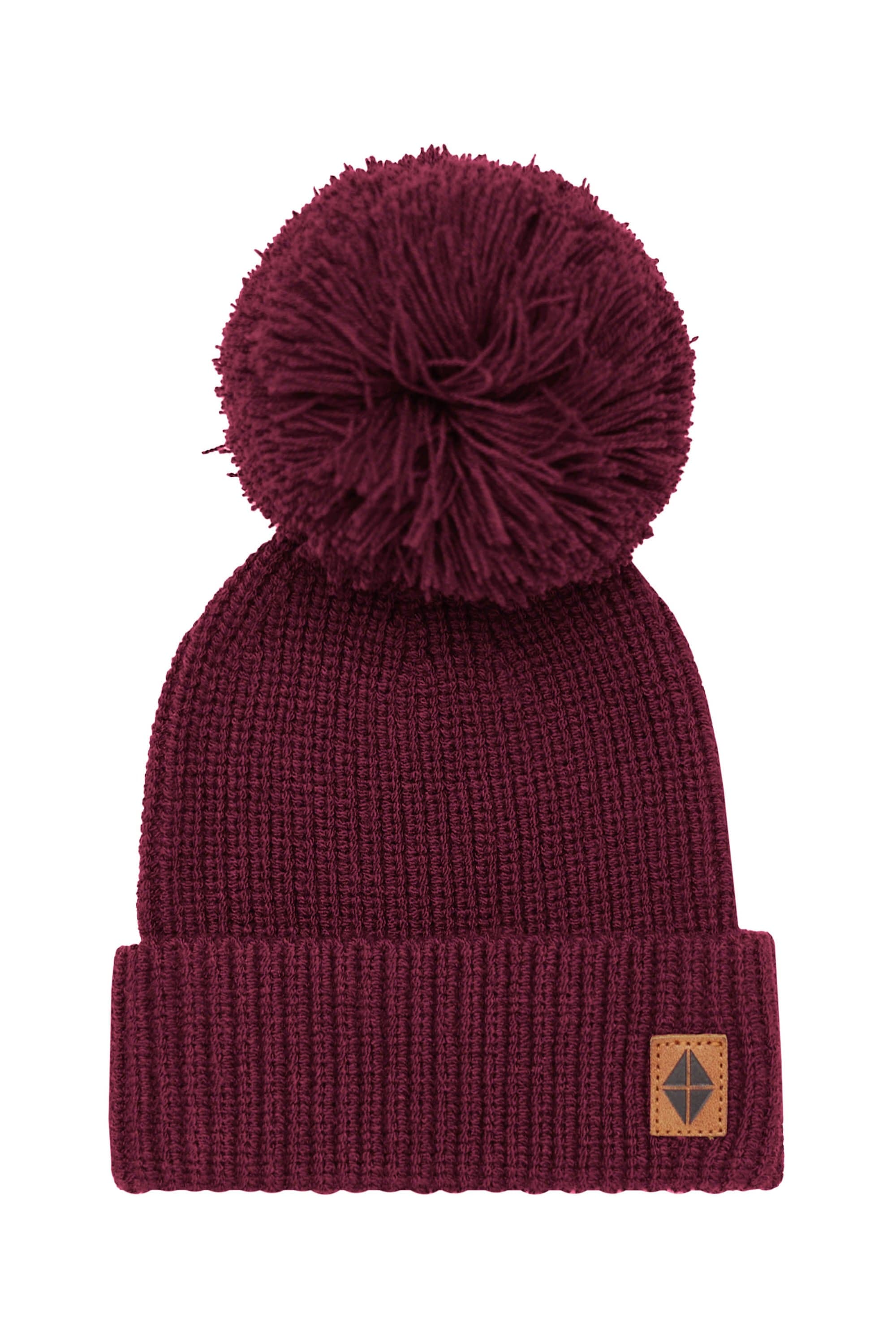 Product of the Chunky Knit Pom Beanie in Burgundy with the Kyte Baby Vegan leather tag visible