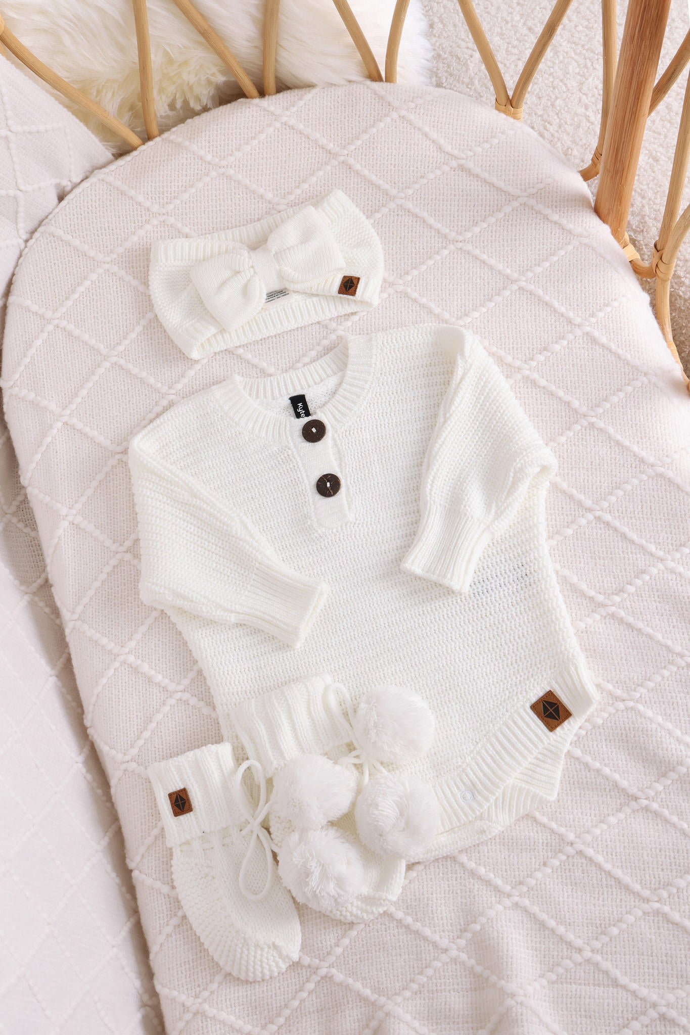 Chunky knit bow headband, chunky knit romper and knit booties in cloud laid in a crib