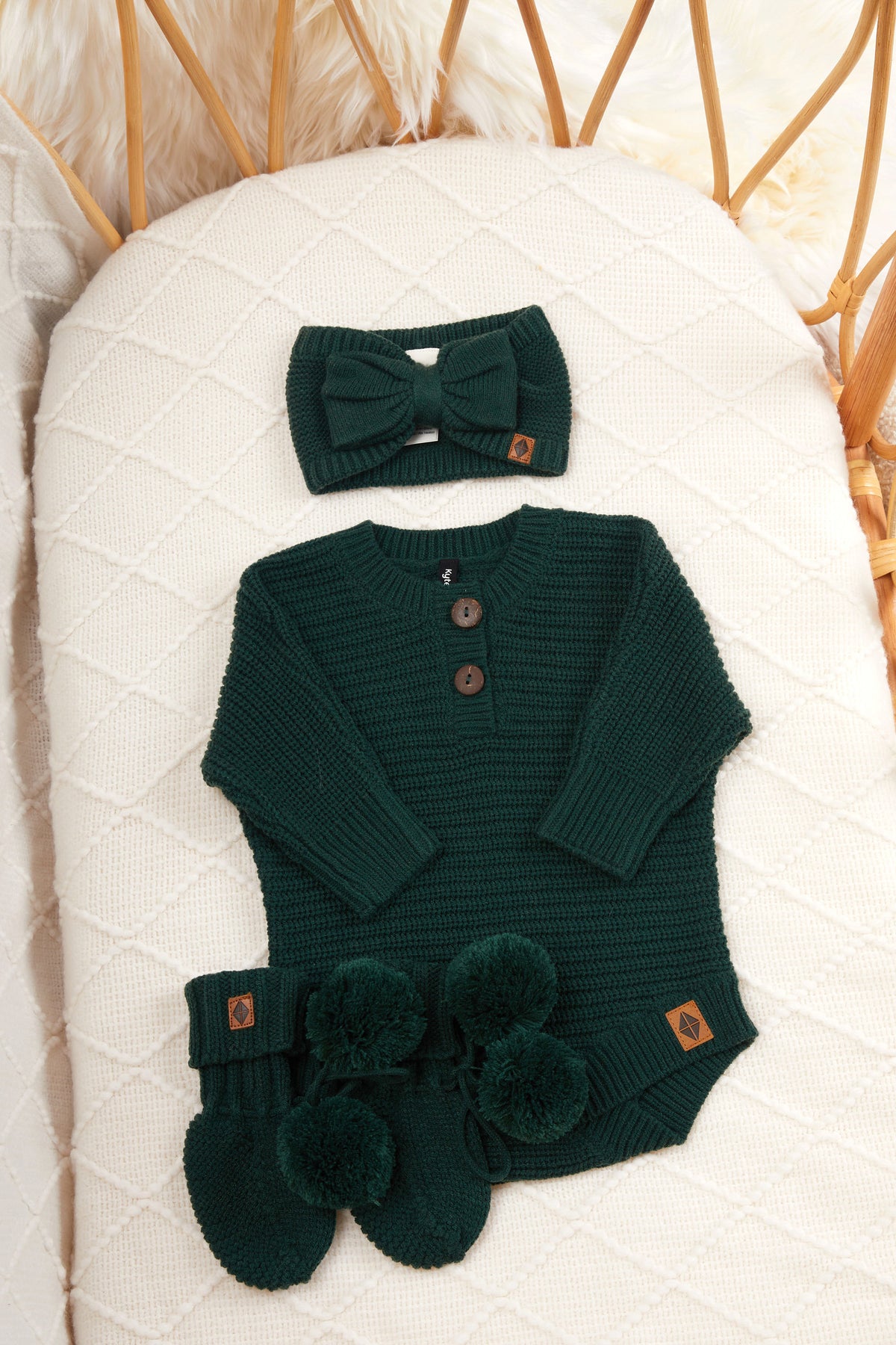 Chunky knit bow headband, chunky knit romper and knit booties in cypress laid in a crib