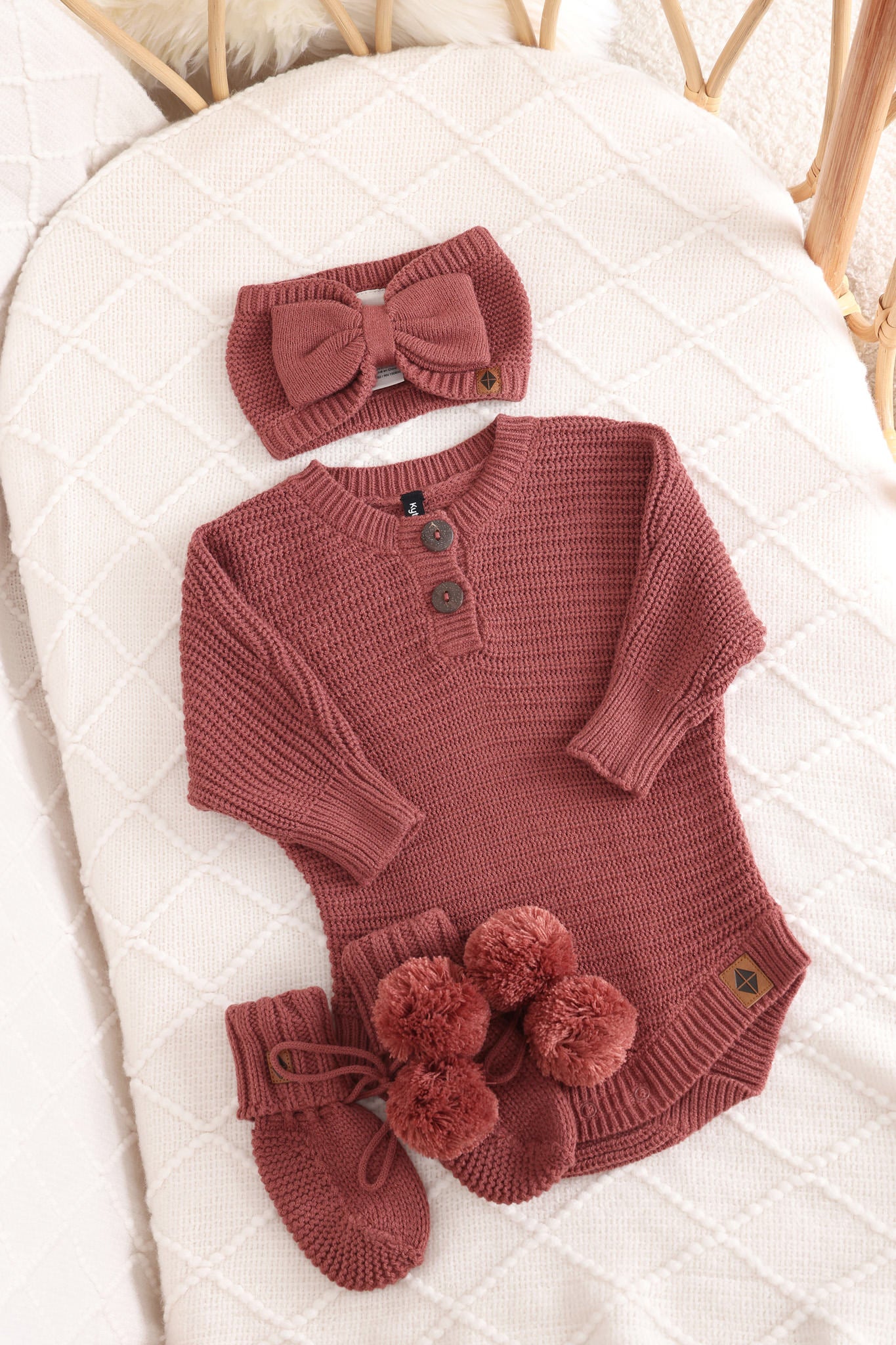 Chunky knit bow headband, chunky knit romper and knit booties in ember laid in a crib