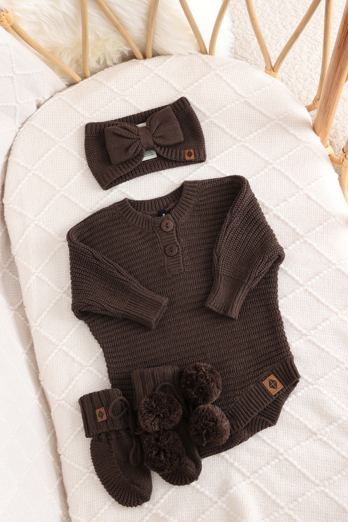Chunky knit bow headband, chunky knit romper and knit booties in espresso laid in a crib