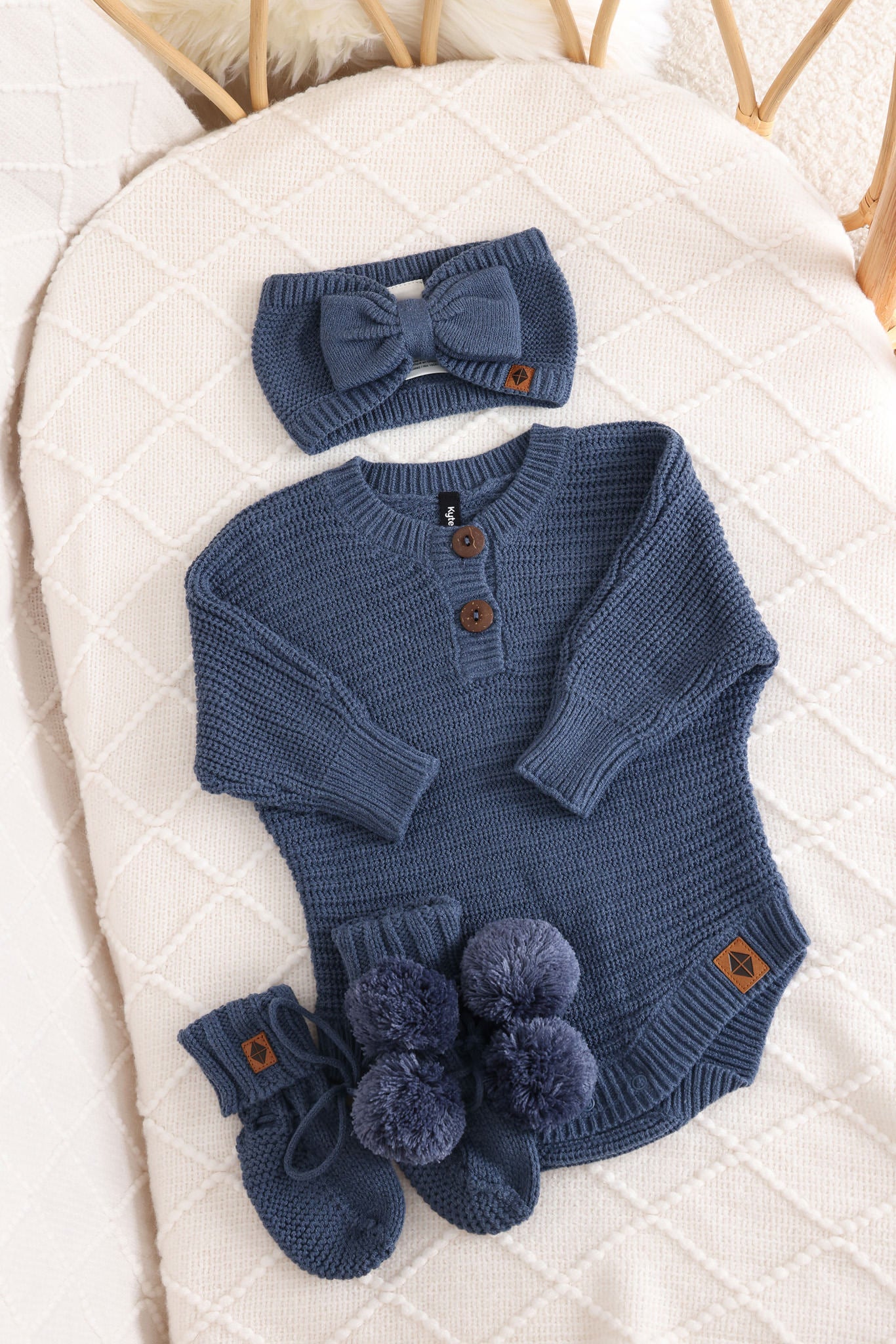 Chunky knit bow headband, chunky knit romper and knit booties in oxford laid in a crib