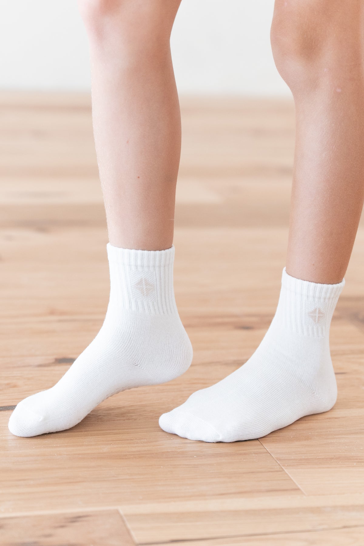 A close-up of a person's feet wearing plain white ankle socks on a light wood floor.