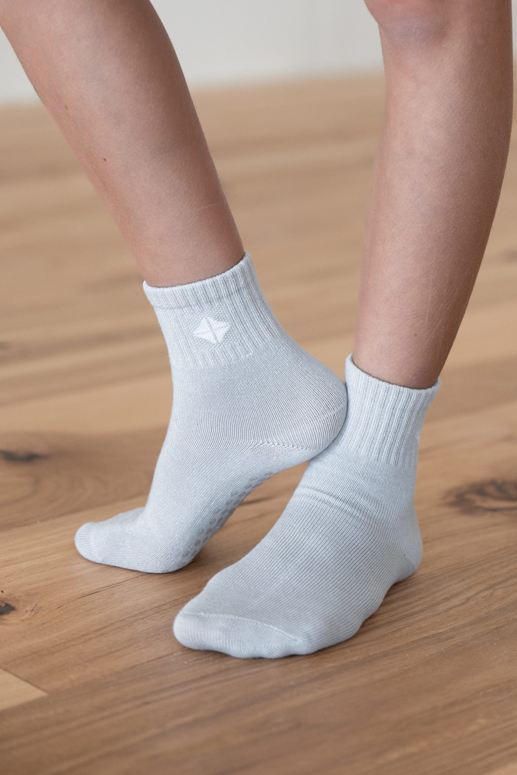 A close-up of a person's feet wearing light grey ribbed ankle socks on a light wood floor.