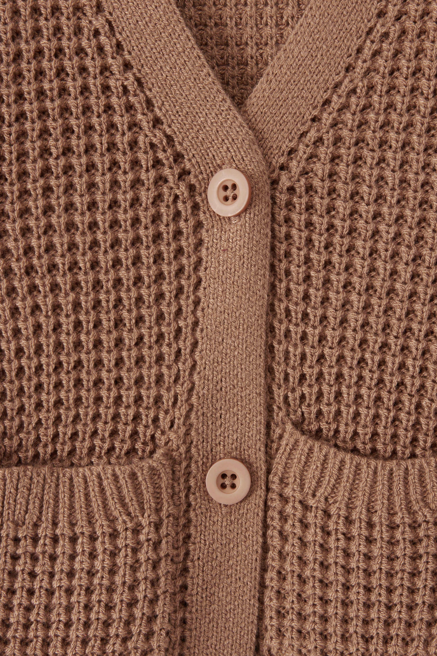 Close-up of a textured knit cardigan in latte color, featuring a waffle-weave pattern, ribbed trim, and two white buttons.