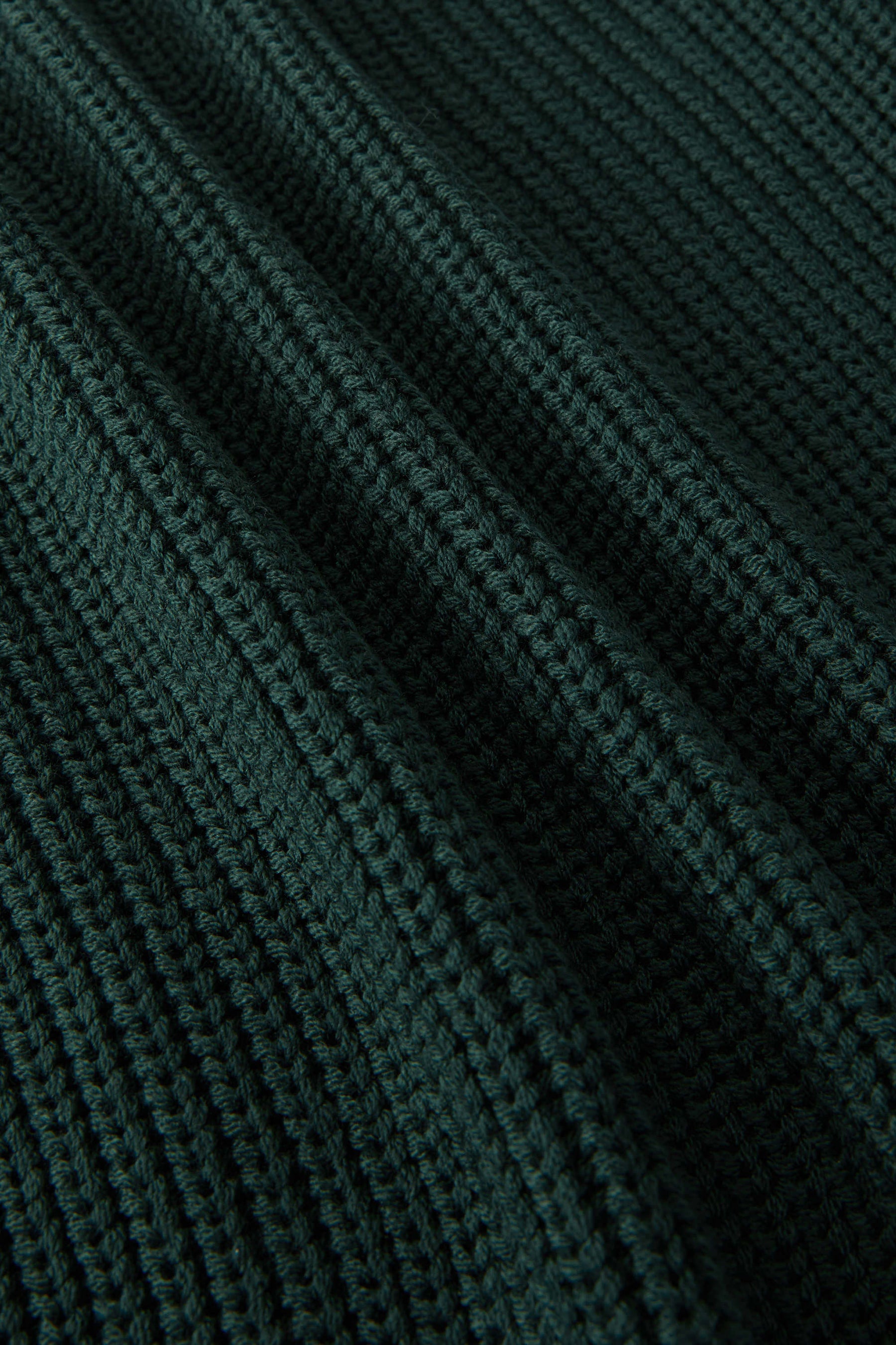 Close-up of a dark forest green ribbed knit fabric texture with a fine waffle pattern.