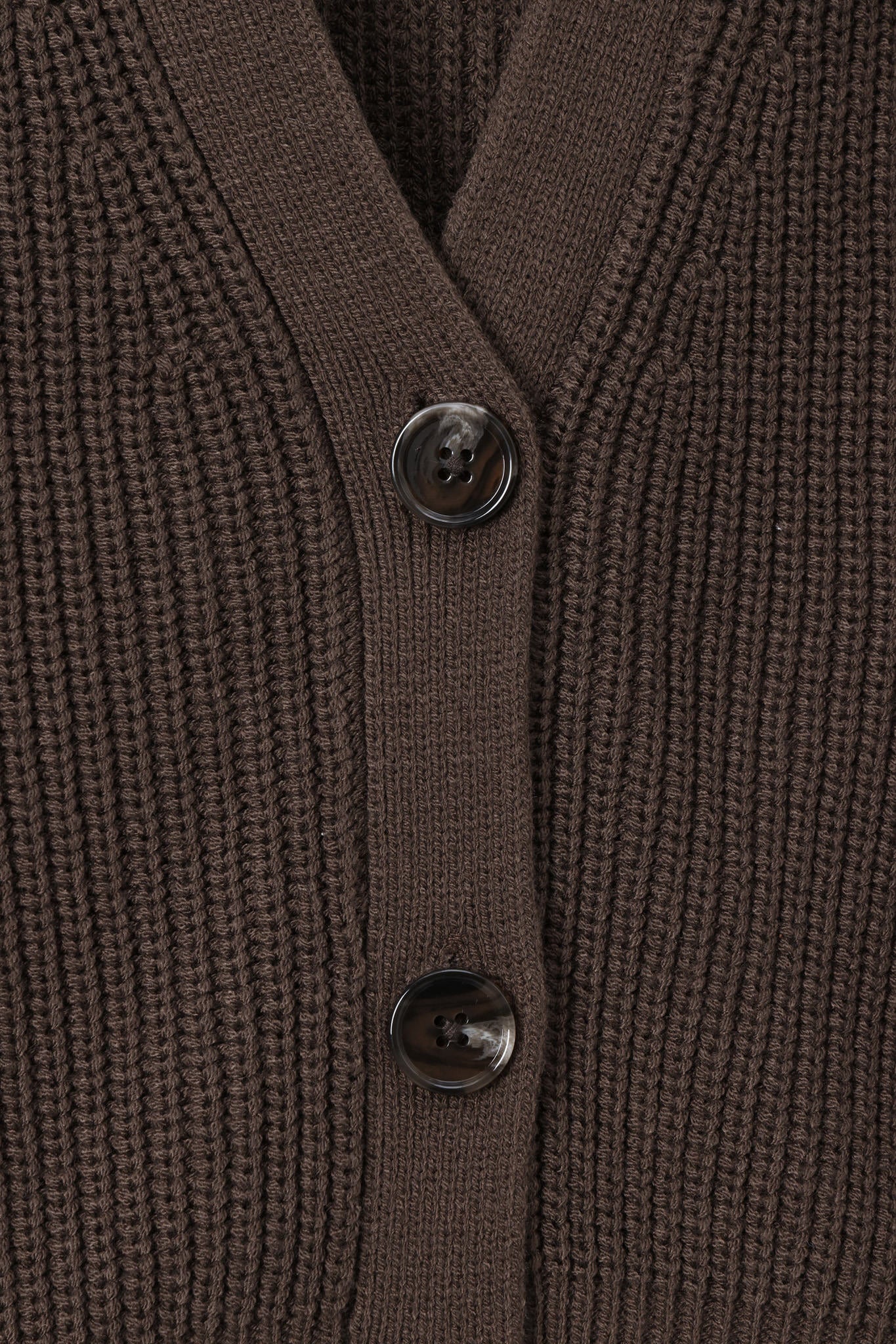 Close-up of a ribbed knit cardigan in dark brown with two dark buttons on a matching brown background.
