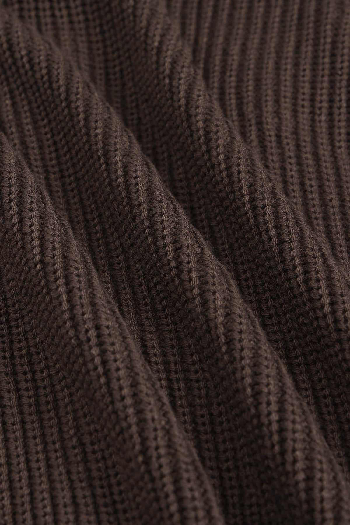Close-up of a dark brown ribbed knit fabric texture with soft folds and a fine woven pattern.