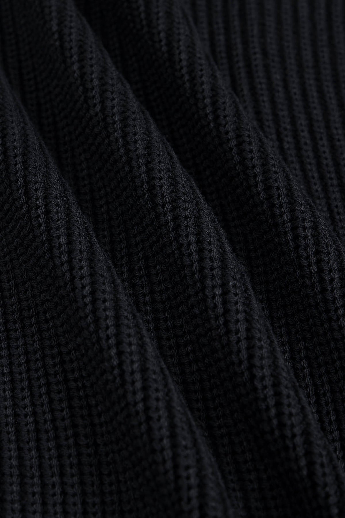 Close-up of a black ribbed knit fabric texture with soft diagonal folds.