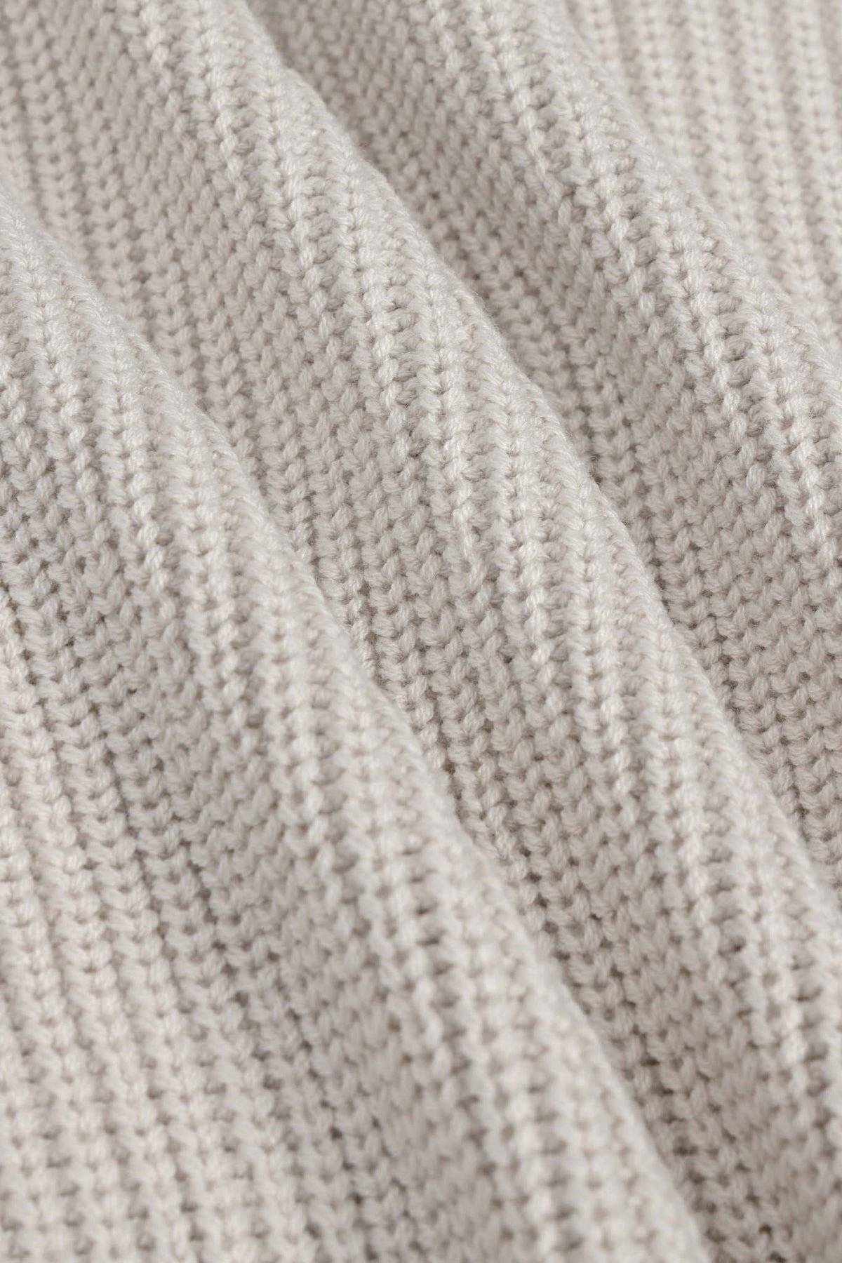 Close-up of a ribbed knit fabric in a light oatmeal beige color, showing the detailed texture and folds of the yarn.