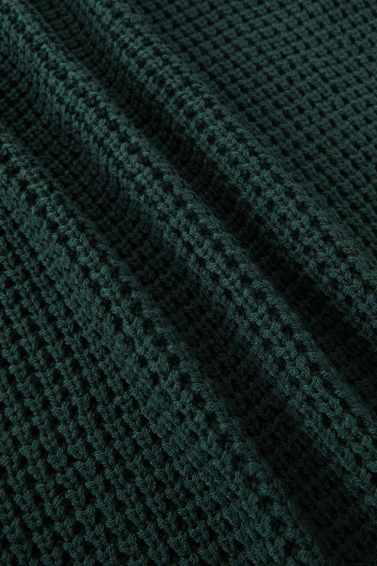 Close-up of a dark forest green waffle-knit fabric texture with soft folds.