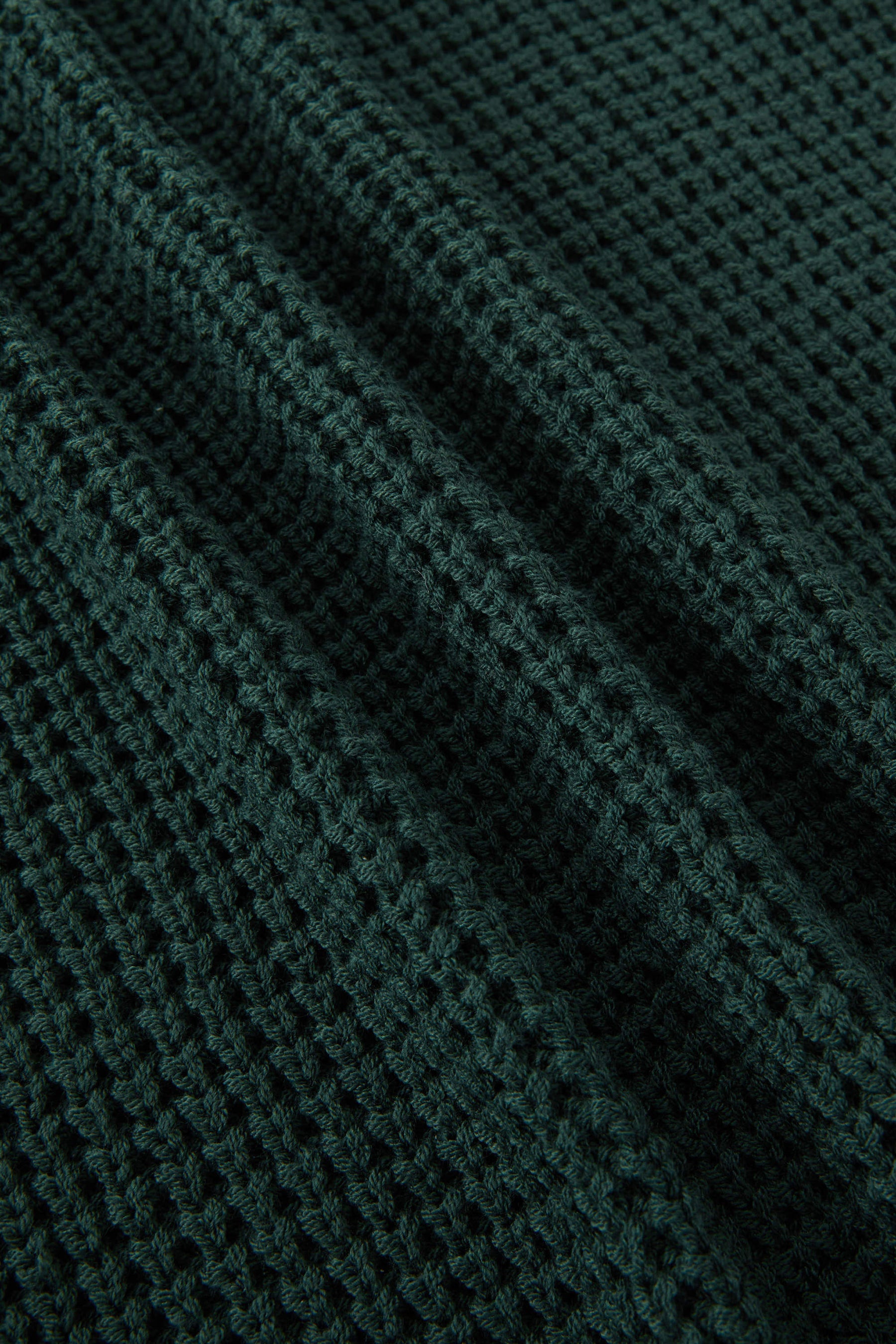 Close-up of a dark forest green waffle-knit fabric texture with soft folds.