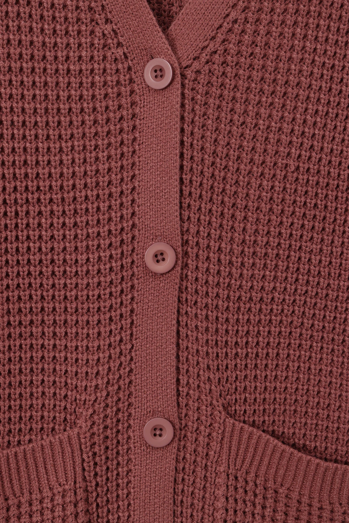 Close-up of a waffle-knit cardigan in a dusty rose or mauve color, featuring a matching button placket and ribbed collar.