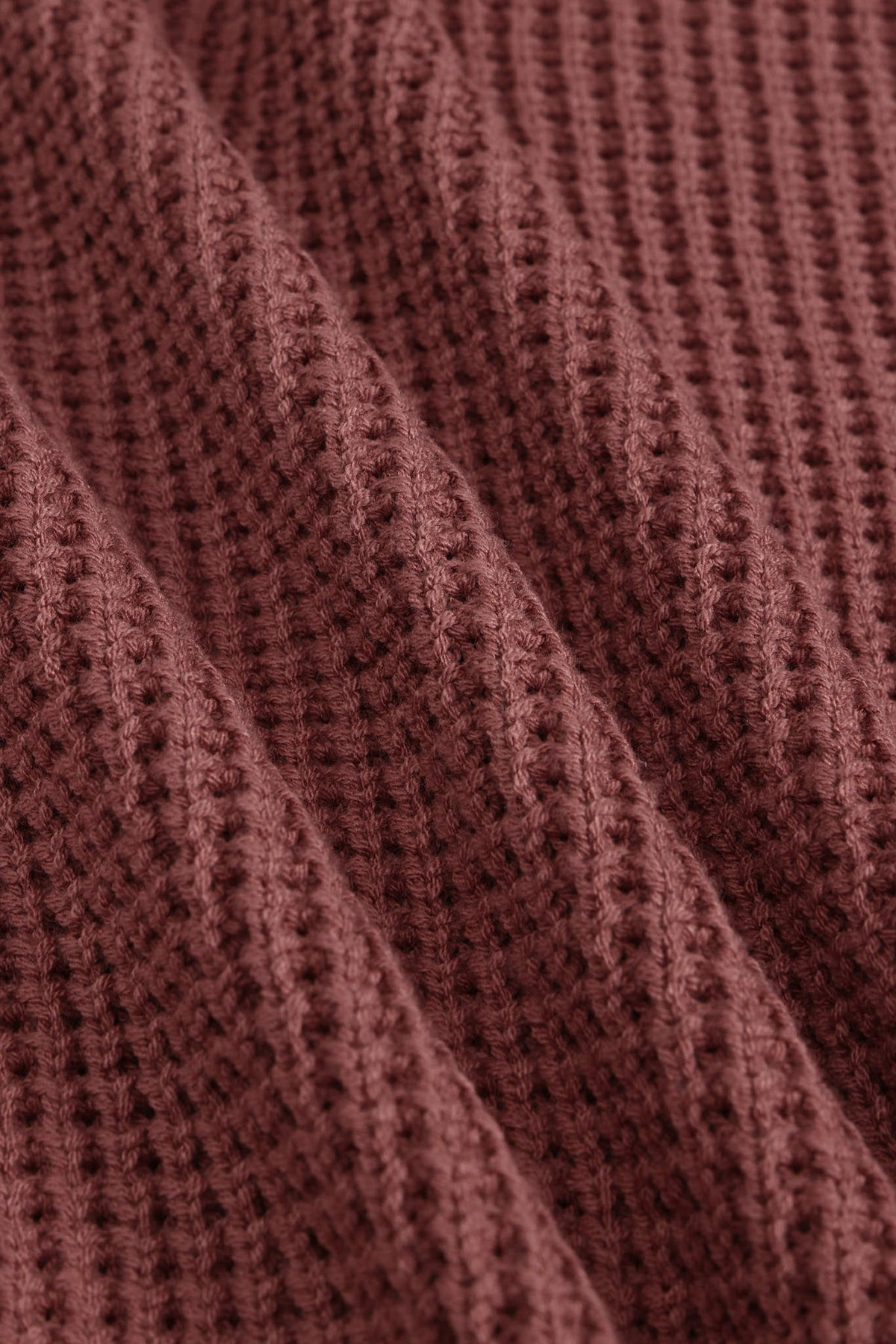 Close-up of a textured knit fabric in a muted dusty rose or mauve-brown color, showing the detailed ribbed pattern and soft folds.