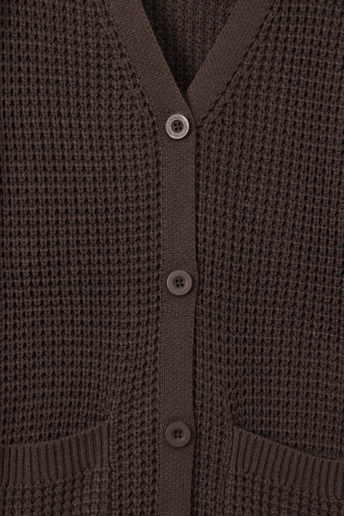 Close-up of a dark brown waffle-knit cardigan sweater showing the buttoned front and ribbed collar, cuffs, and hem.