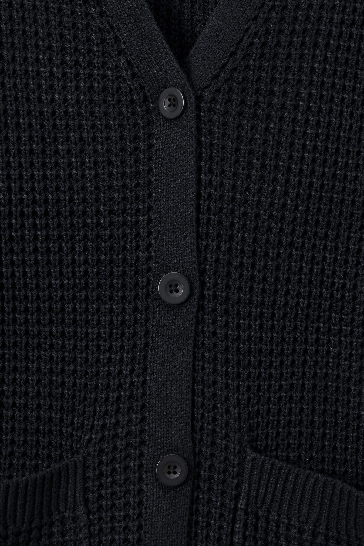 Close-up of a black waffle-knit cardigan sweater showing the button closure and ribbed collar.