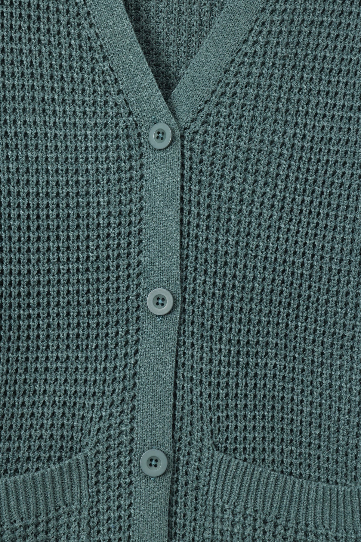 Close-up of a textured knit cardigan in a muted sage green color, featuring a V-neckline, three front buttons, and ribbed trim.