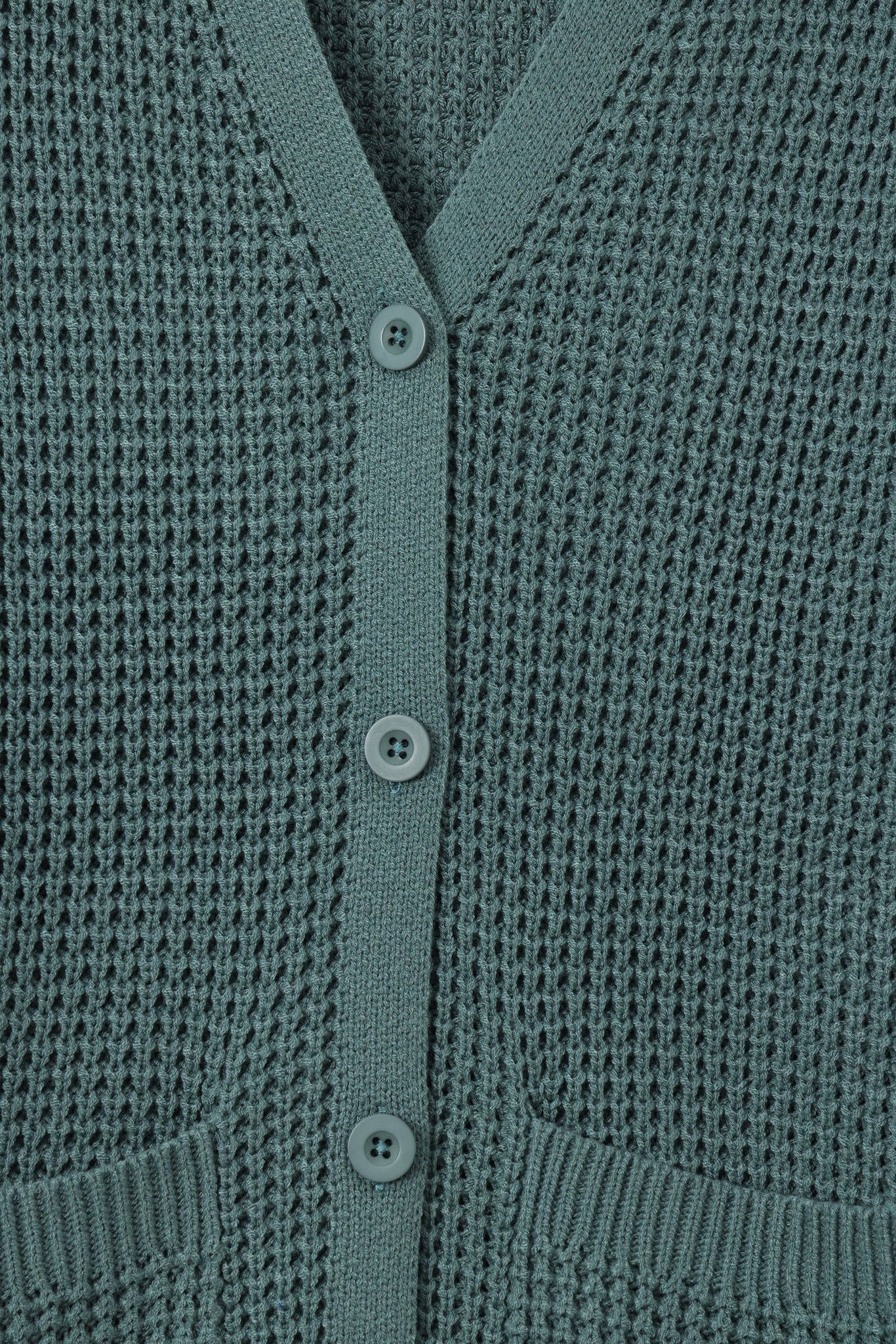 Close-up of a textured knit cardigan in a muted sage green color, featuring a V-neckline, three front buttons, and ribbed trim.