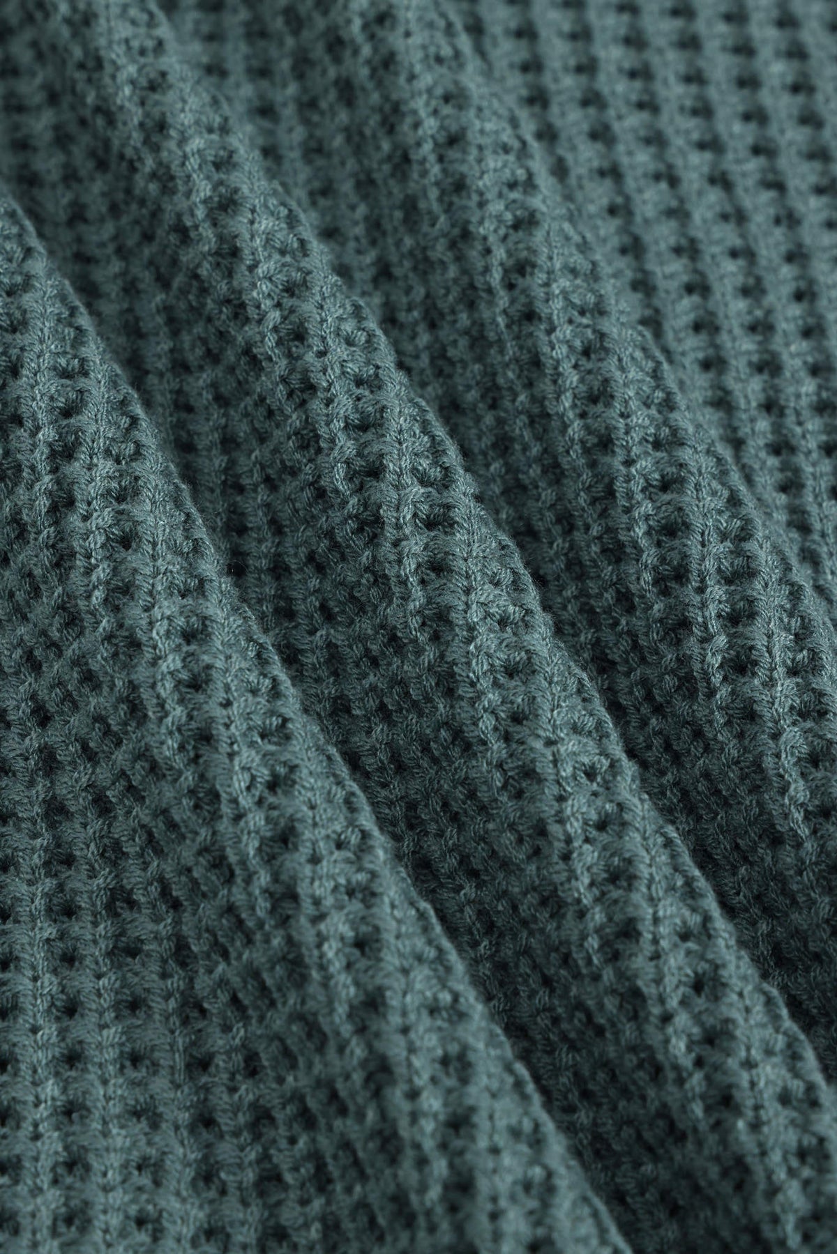 Close-up of a textured knit fabric with a waffle or basketweave pattern in a muted blue-gray color, shown with soft folds.