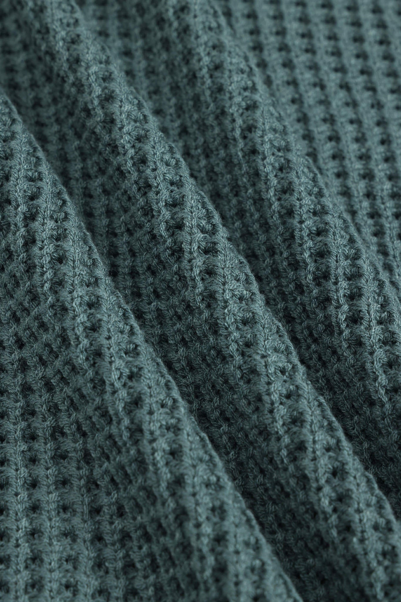 Close-up of a textured knit fabric with a waffle or basketweave pattern in a muted blue-gray color, shown with soft folds.
