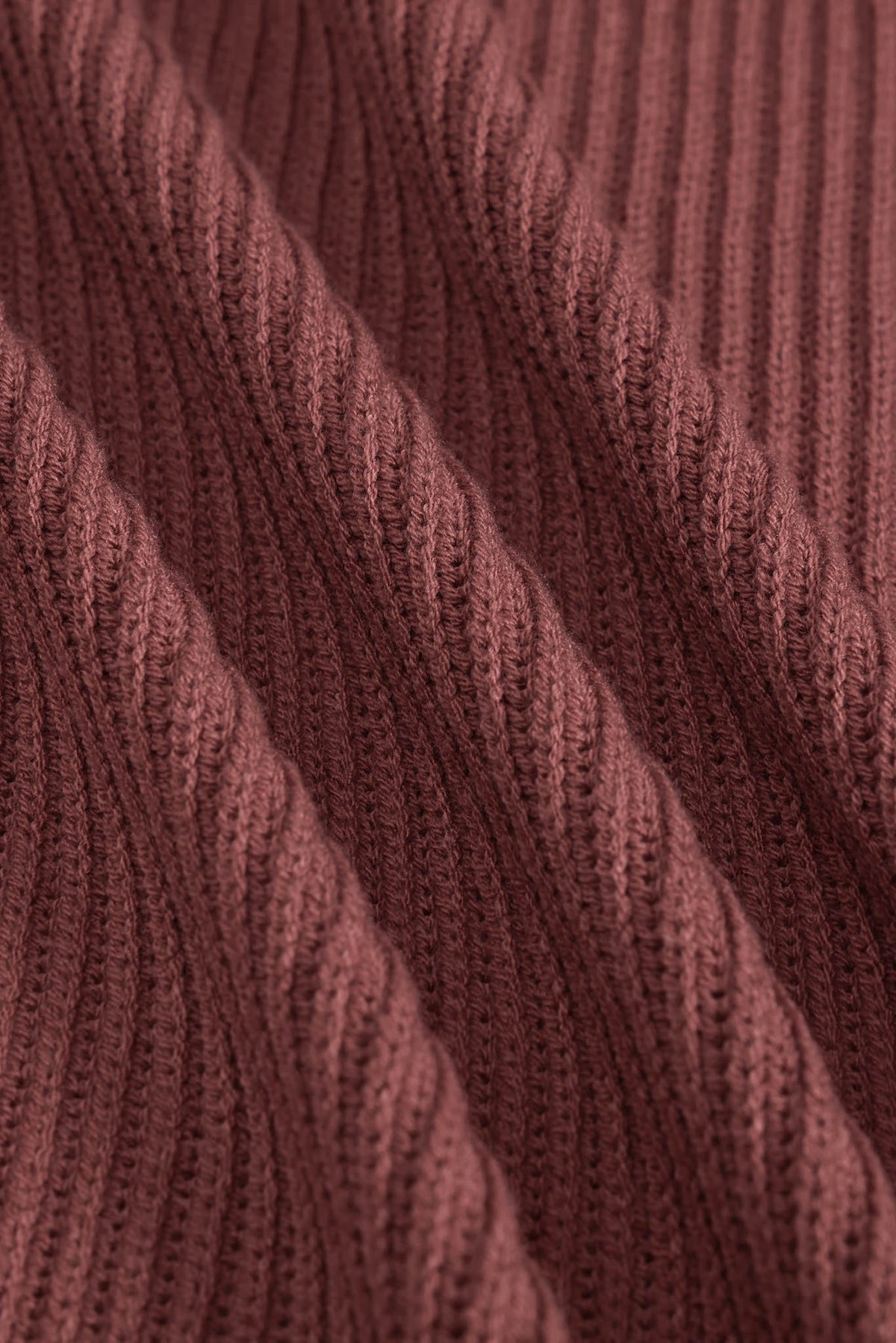 Close-up of a ribbed knit fabric in a dusty rose or mauve-brown color, showing the detailed texture and folds of the yarn.