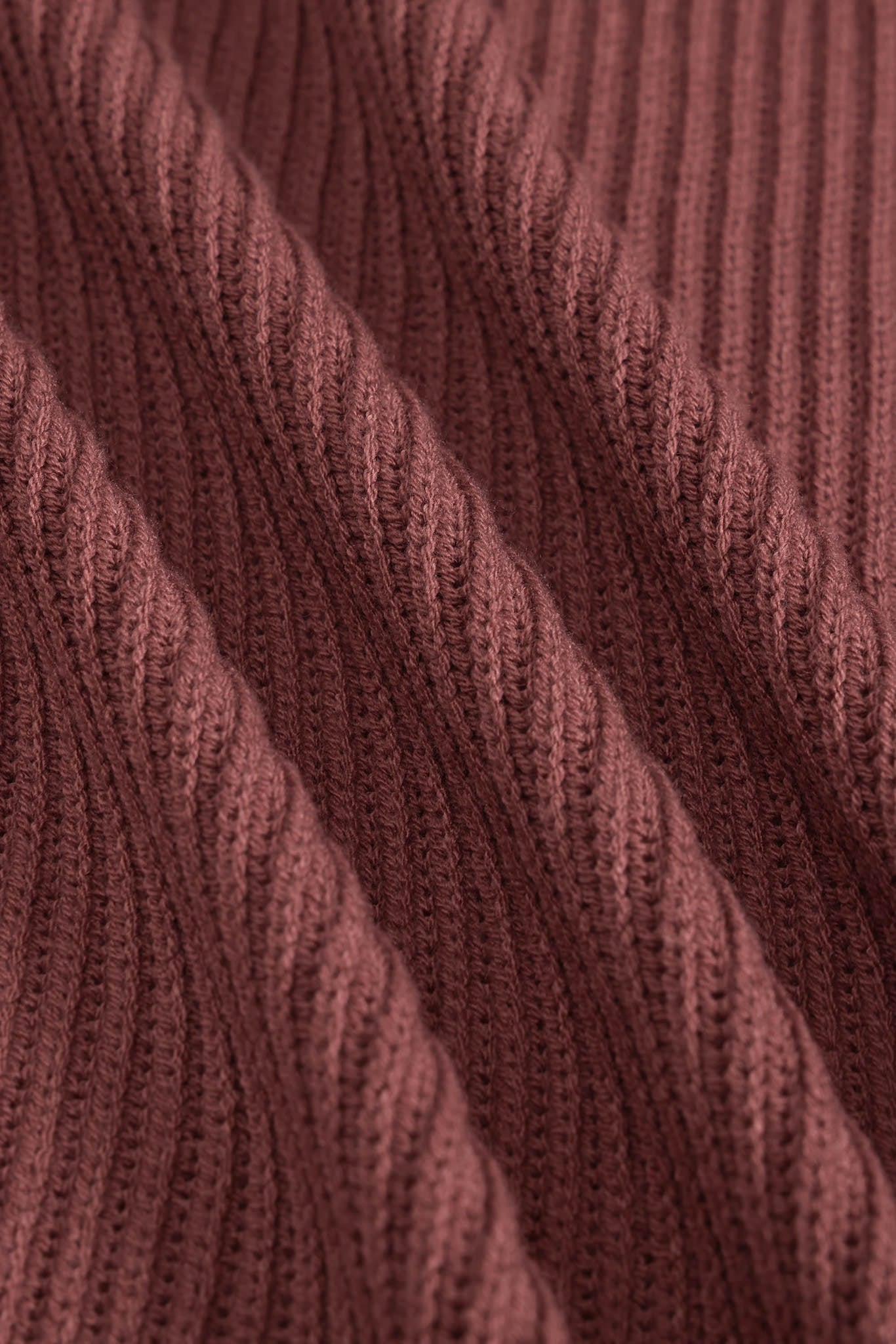 Close-up of a ribbed knit fabric in a dusty rose or mauve-brown color, showing the detailed texture and folds of the yarn.