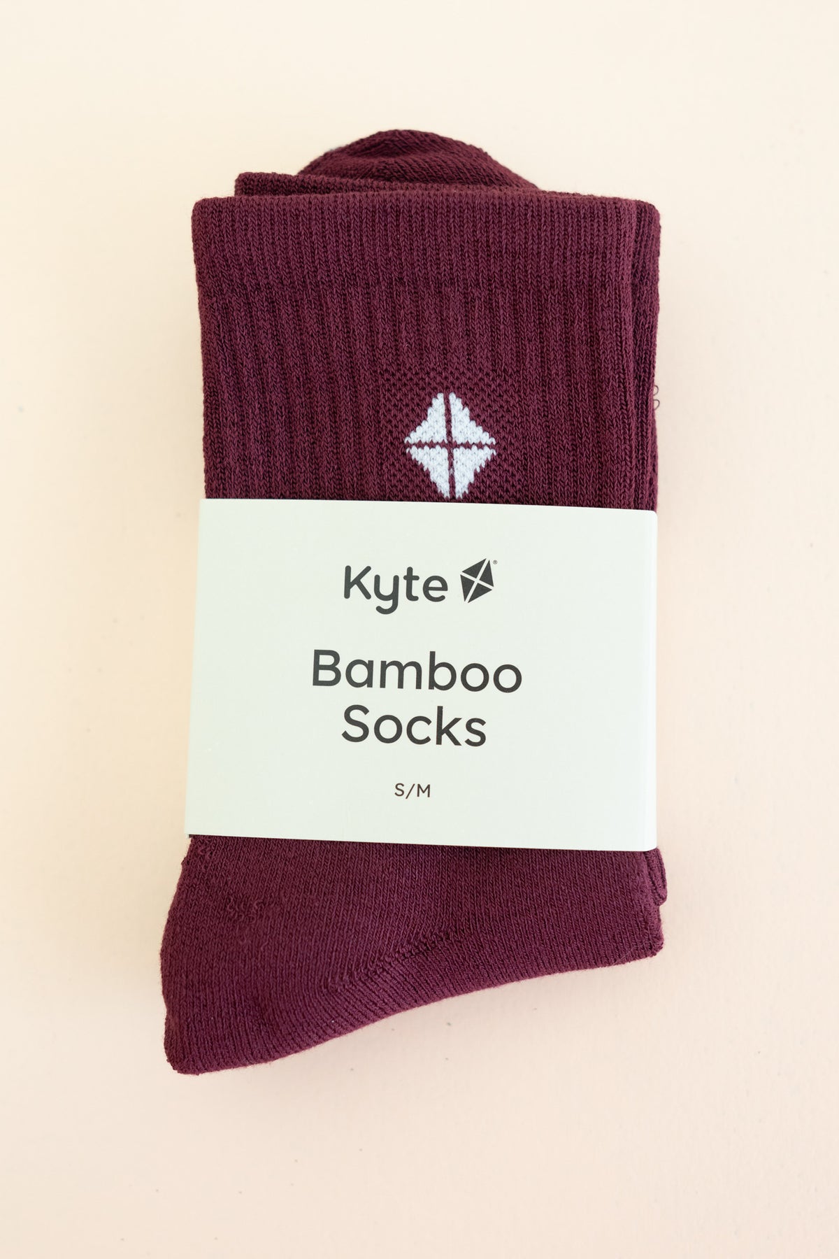 Adult Crew Socks in Burgundy shown in its packaging laying on a light neutral surface