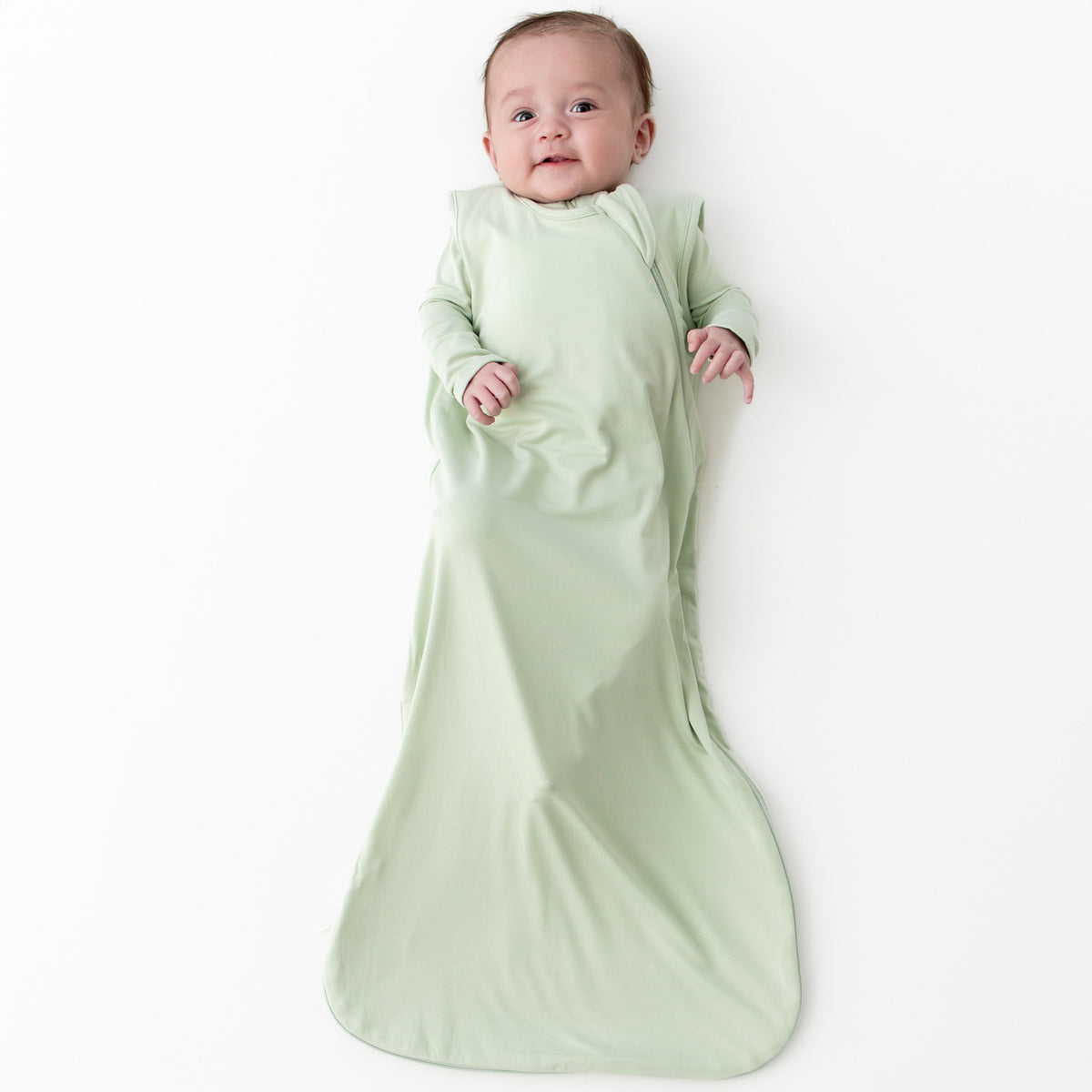 Baby wearing a 0.5 sleep bag in a light green color called Basil