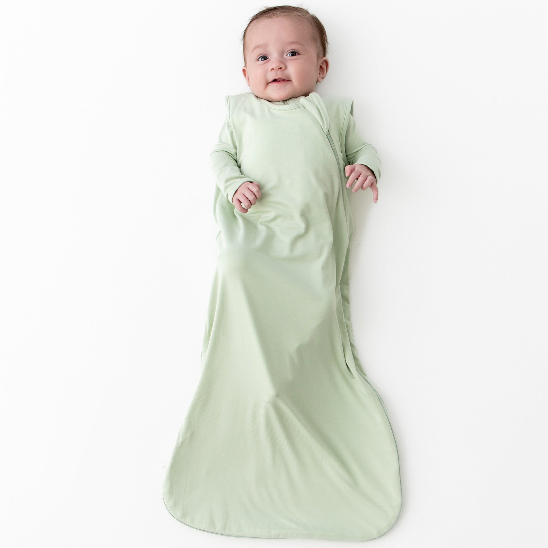 Baby wearing a 0.5 sleep bag in a light green color called Basil