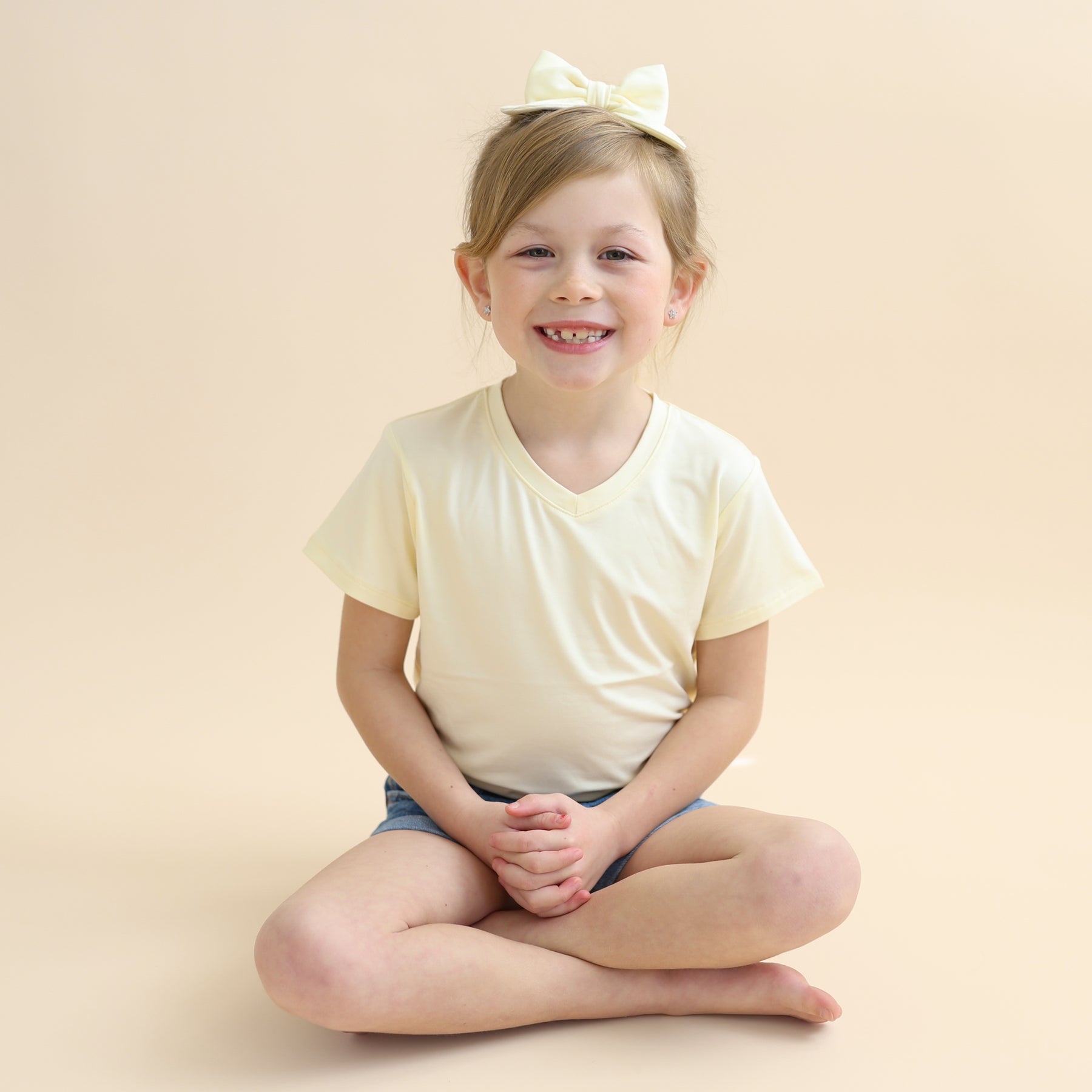 Young smiling girl sitting cross legged on the floor wearing the Medium Alligator Clip Bow in Chamomile with a matching shirt