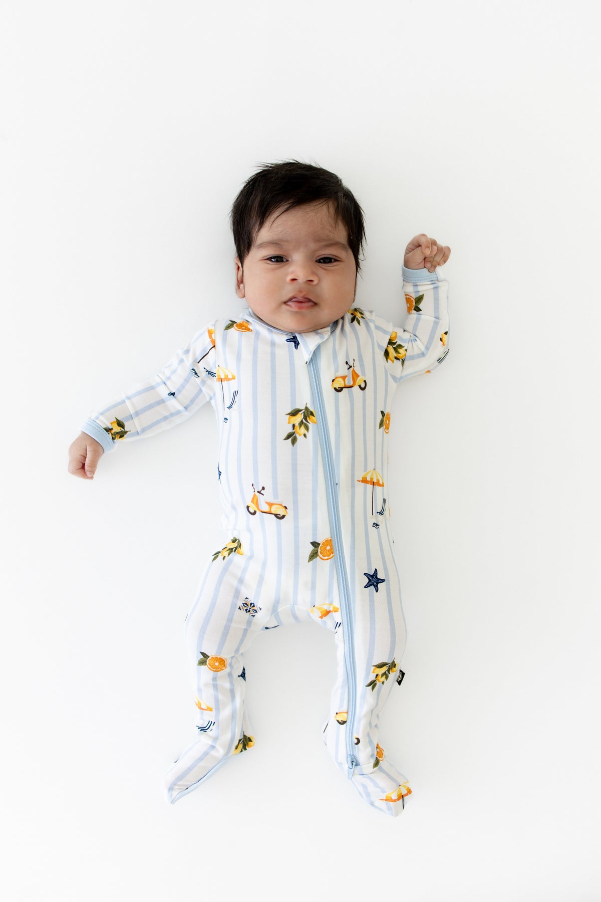 Newborn laying on a white surface wearing the Zippered Footie in Amalfi Coast