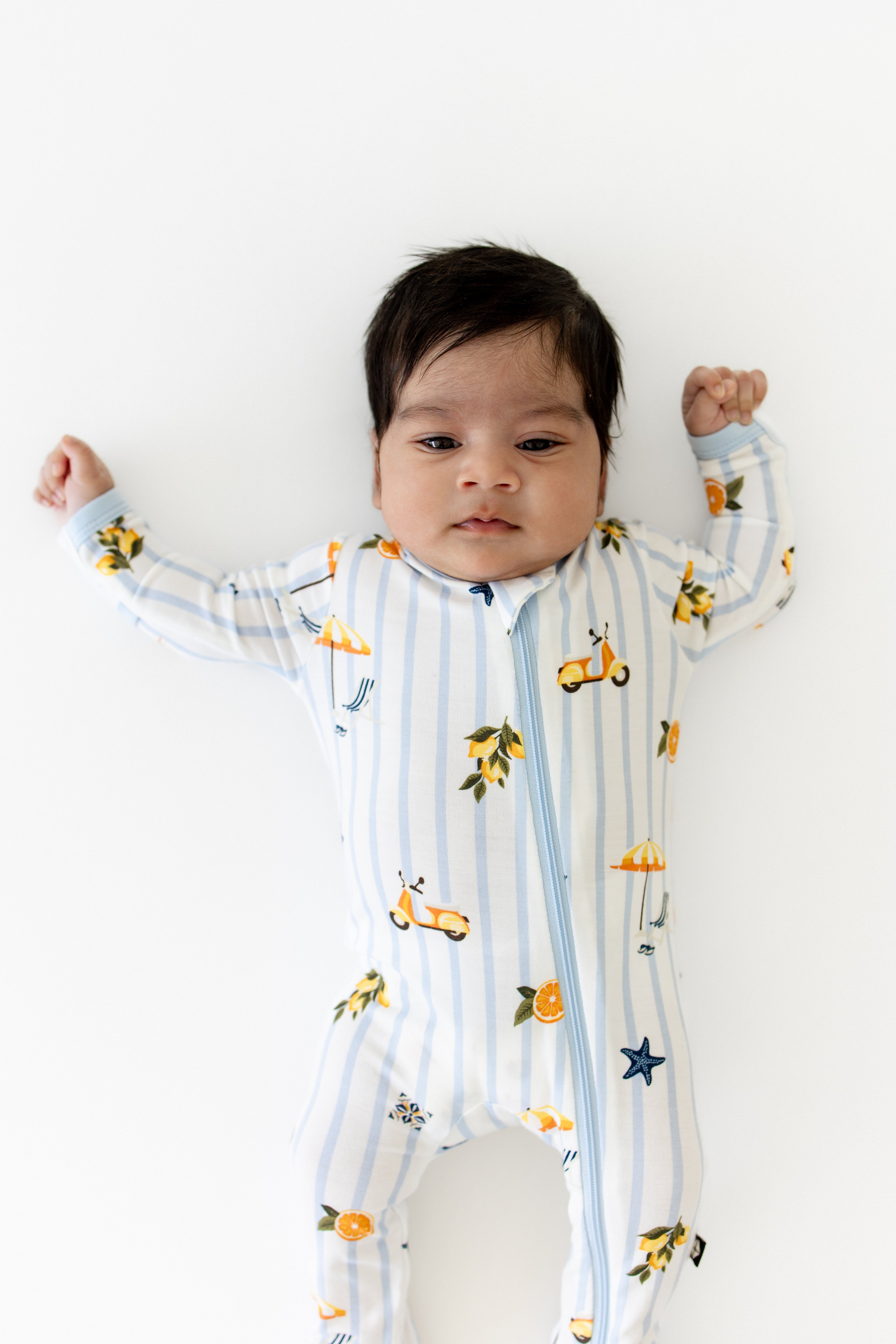 Close up of newborn wearing the Zippered Footie in Amalfi Coast laying on a white surface