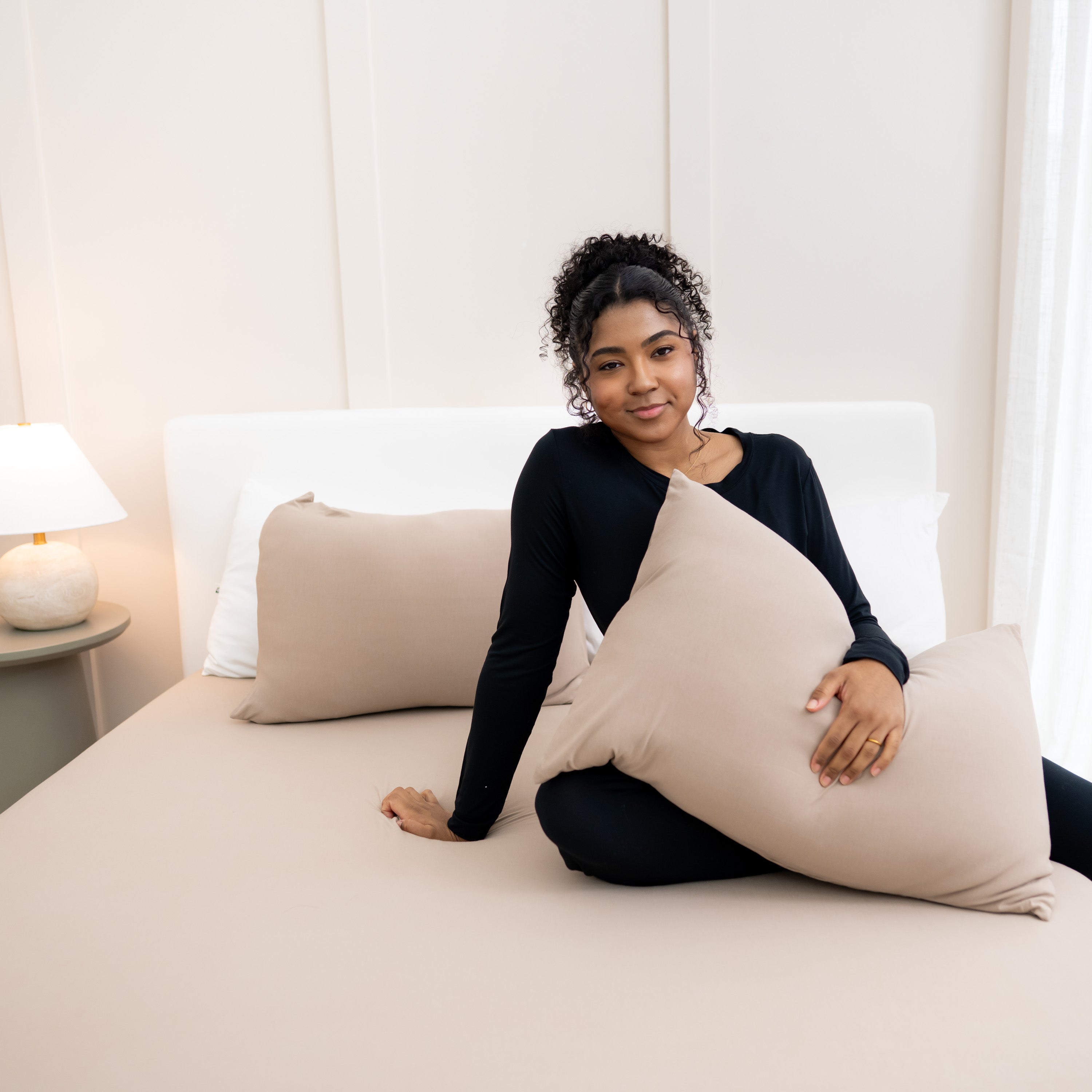 Model sitting on bed with Fitted Sheet with Pillowcases in Almond