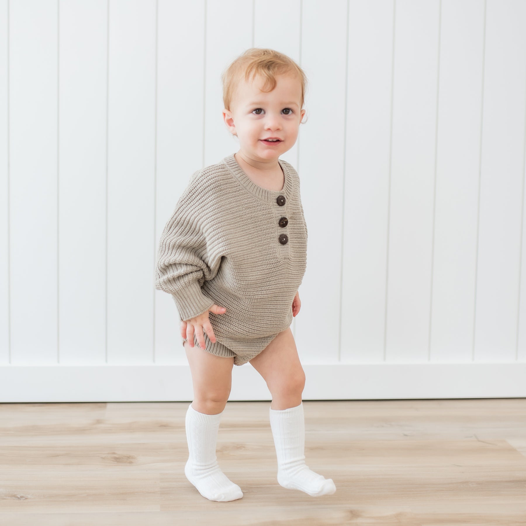 Toddler walking wearing the Chunky Knit Romper in Almond and Cloud Knee high socks