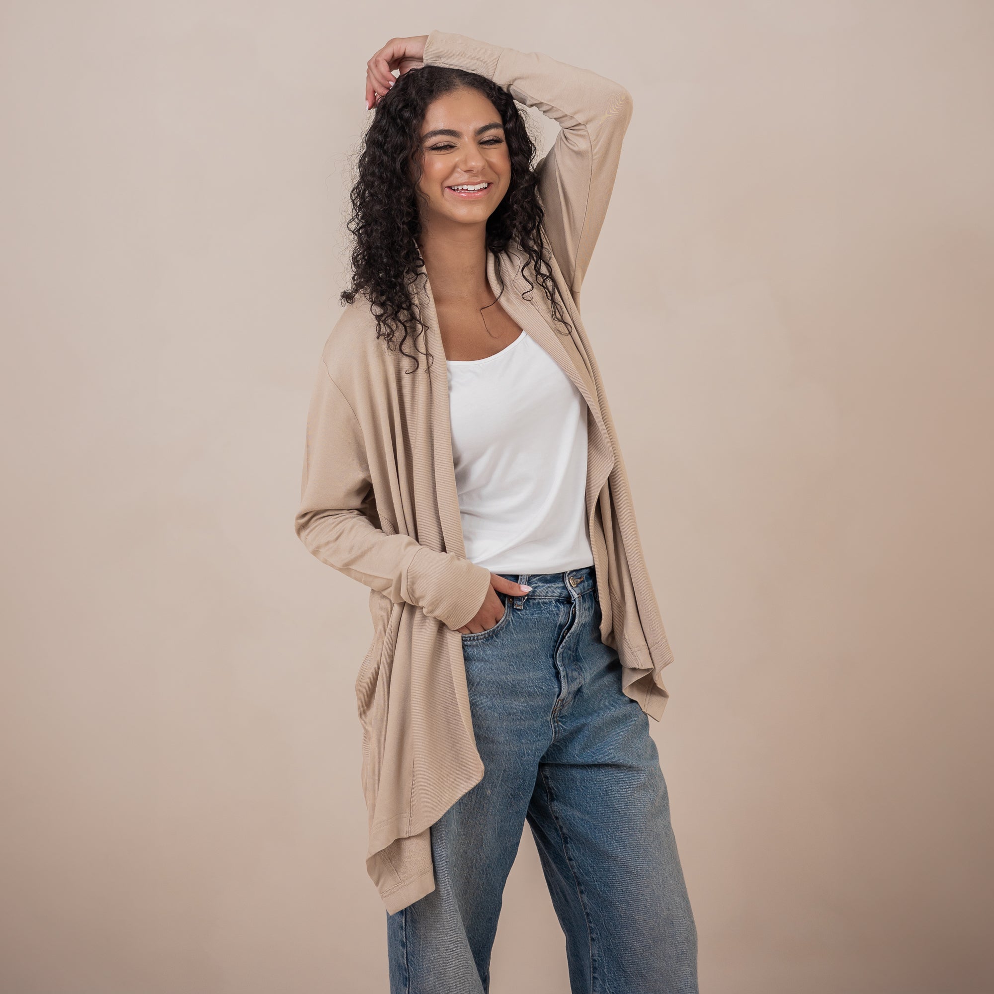 Smiling model standing with one hand in her jeans pocket with the other hand on her head wearing the Women's French Terry Wrap Top in Almond 