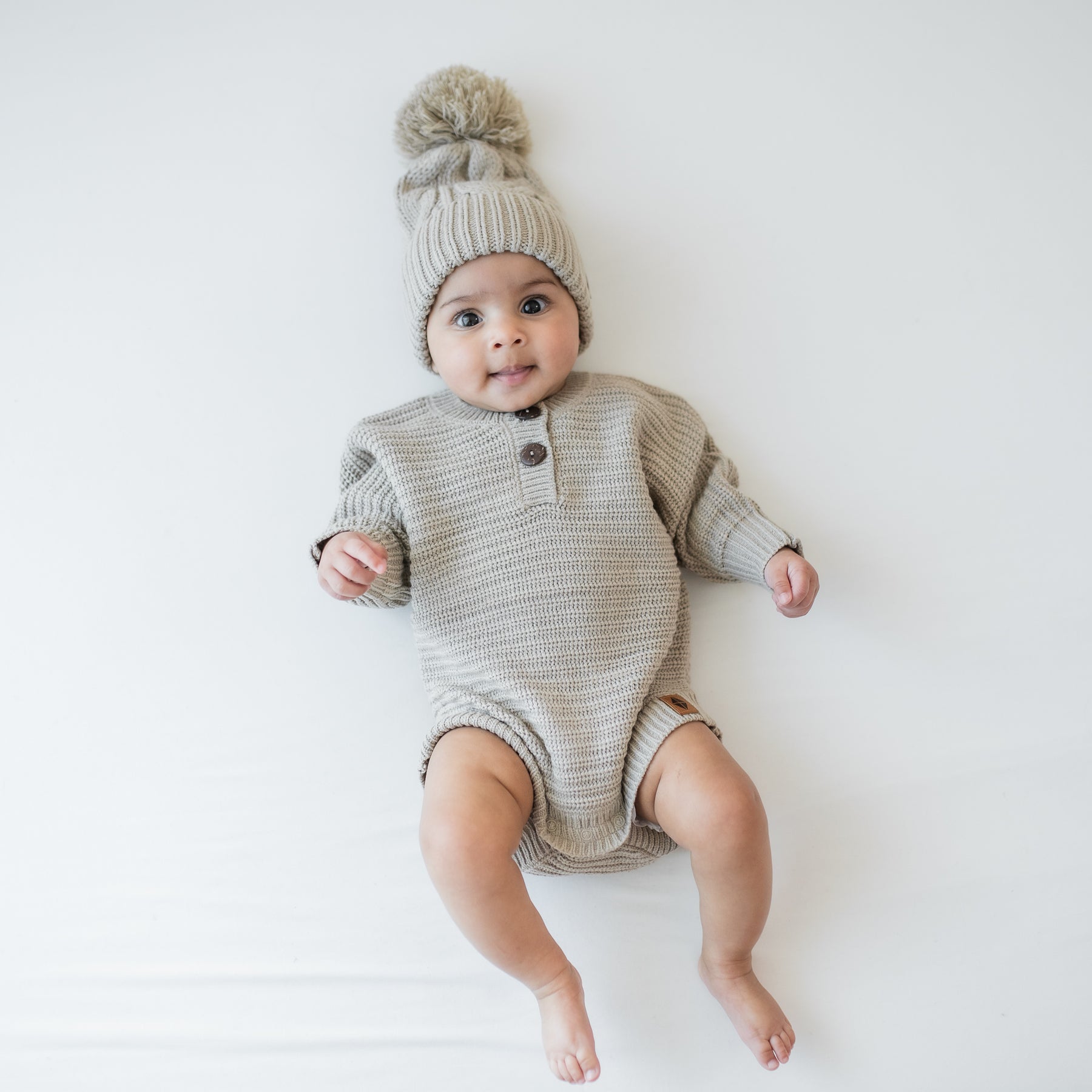 Infant wearing the Chunky Cable Knit Beanie in Almond and matching chunky knit romper