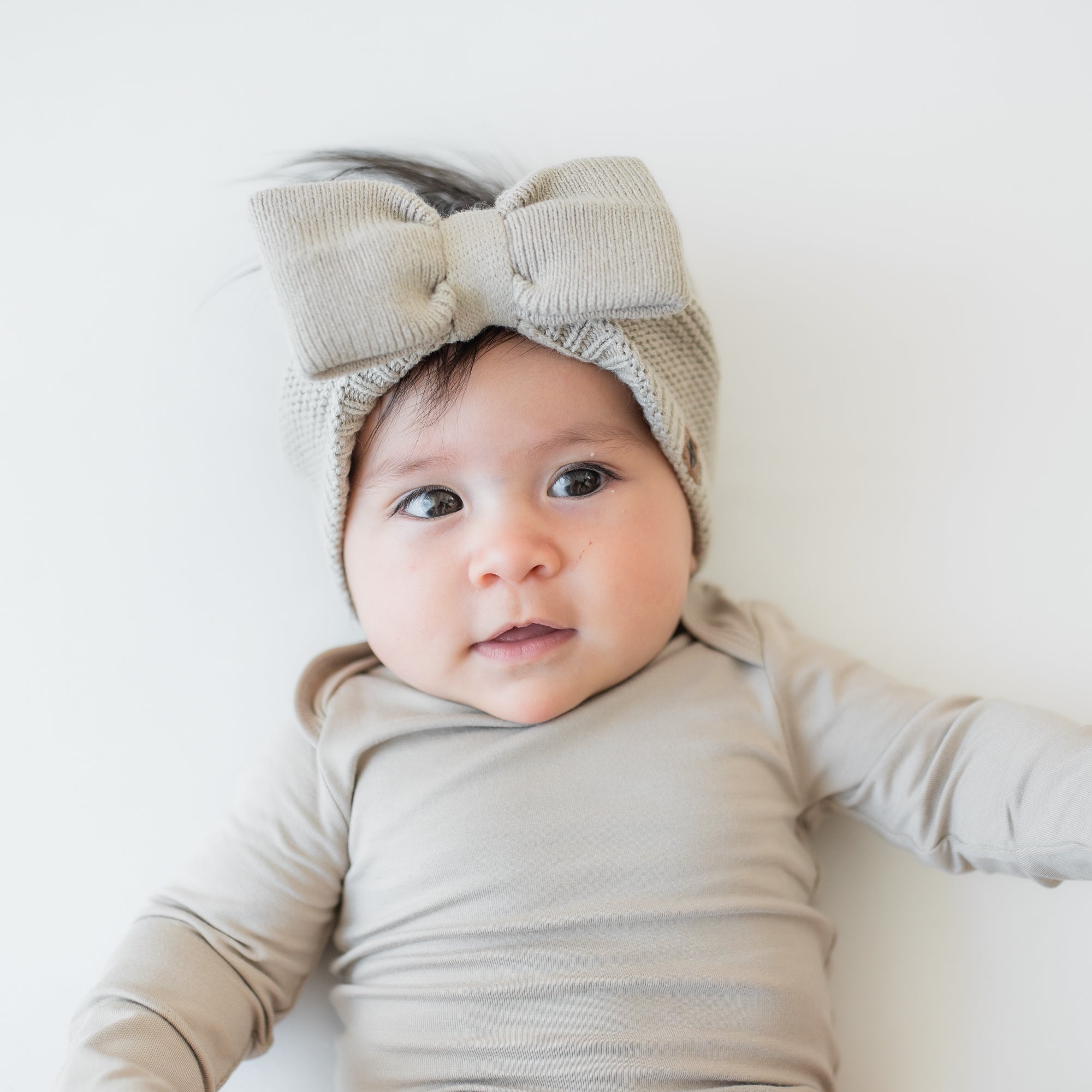 Close up of the Chunky Knit Bow Headband in Almond shown on an infant wearing a matching long sleeve bodysuit