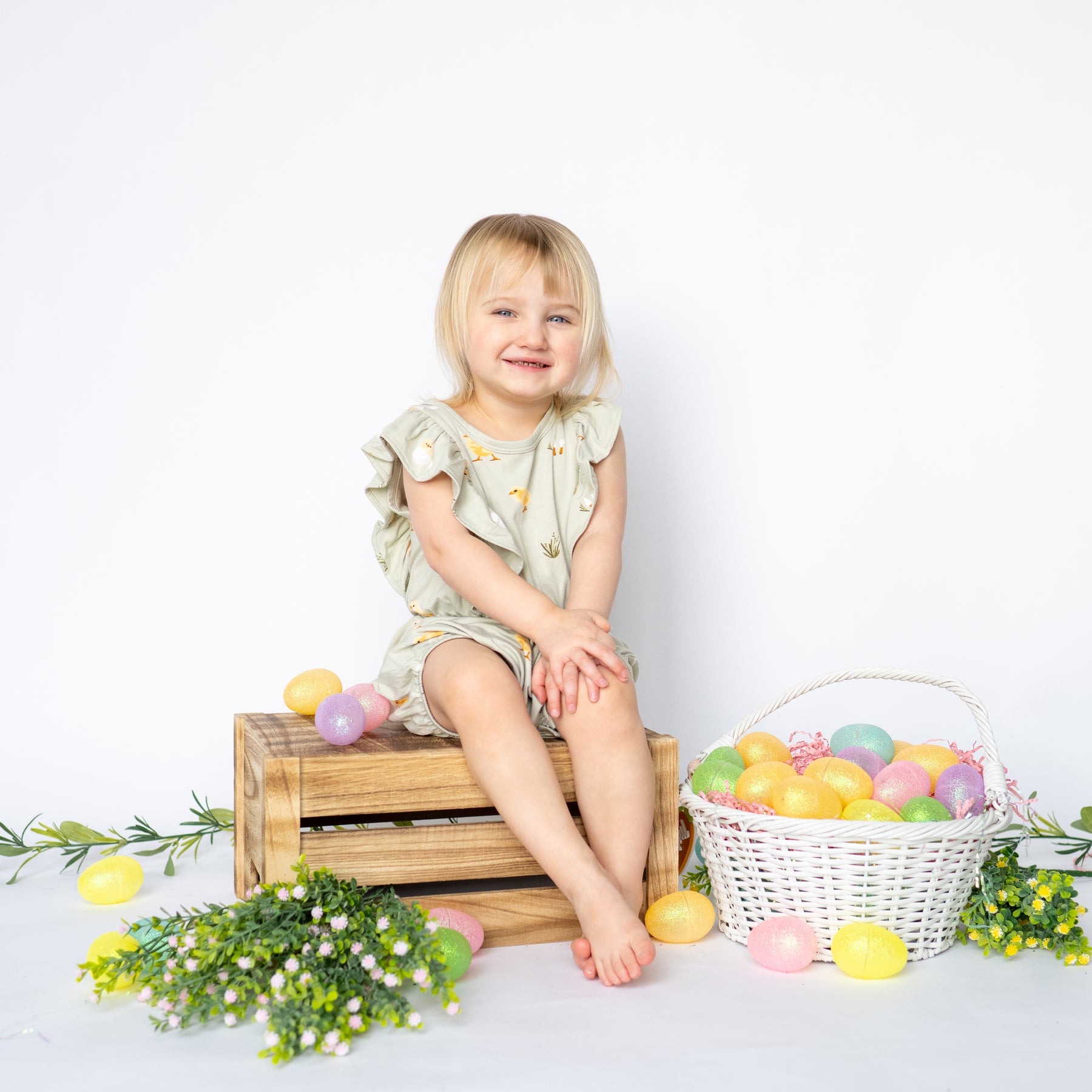 Toddler sitting in Bubble Romper in Aloe Chick by easter eggs