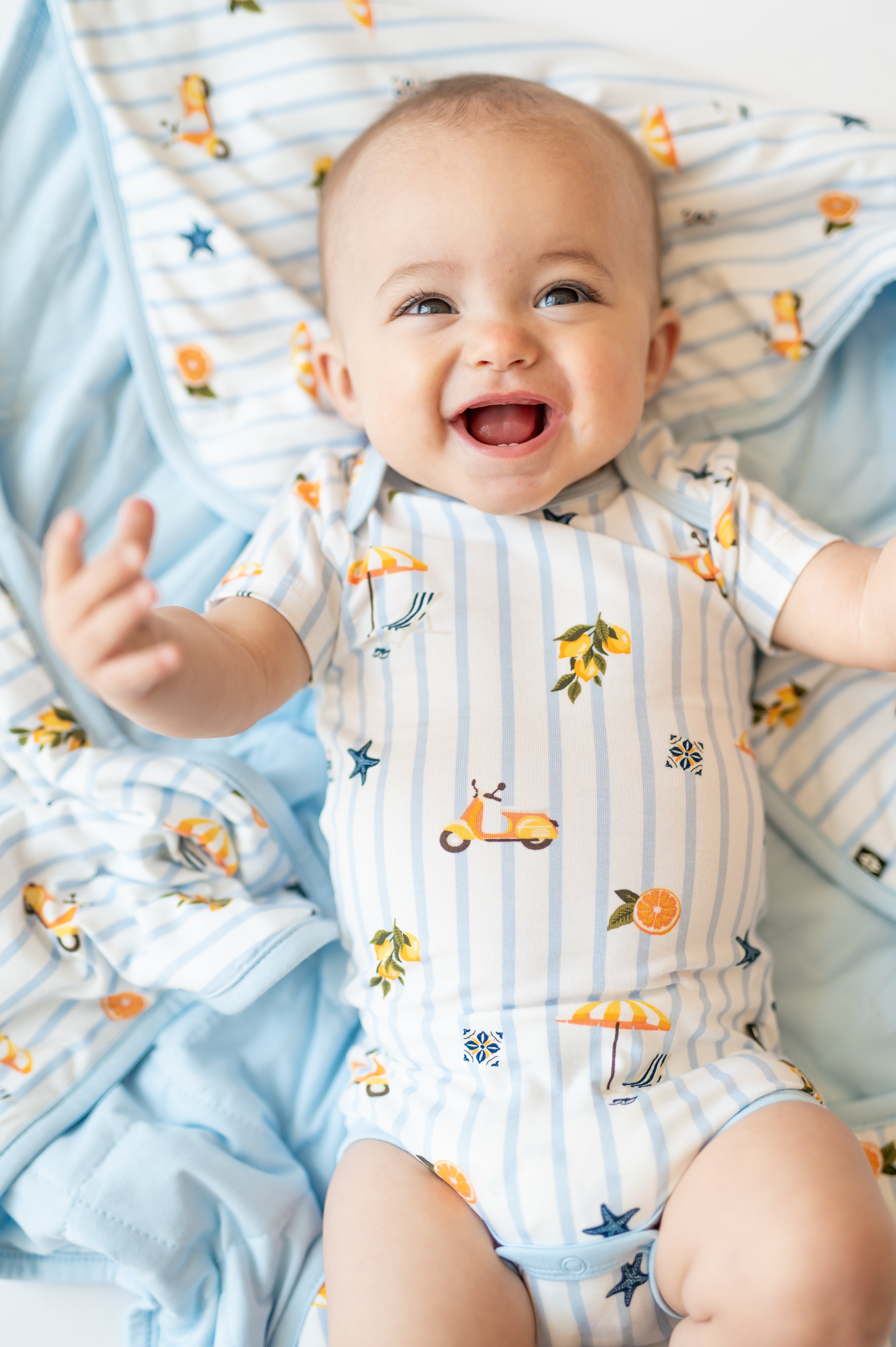 Close up of infant wearing the Bodysuit in Amalfi Coast print lying on a matching baby blanket