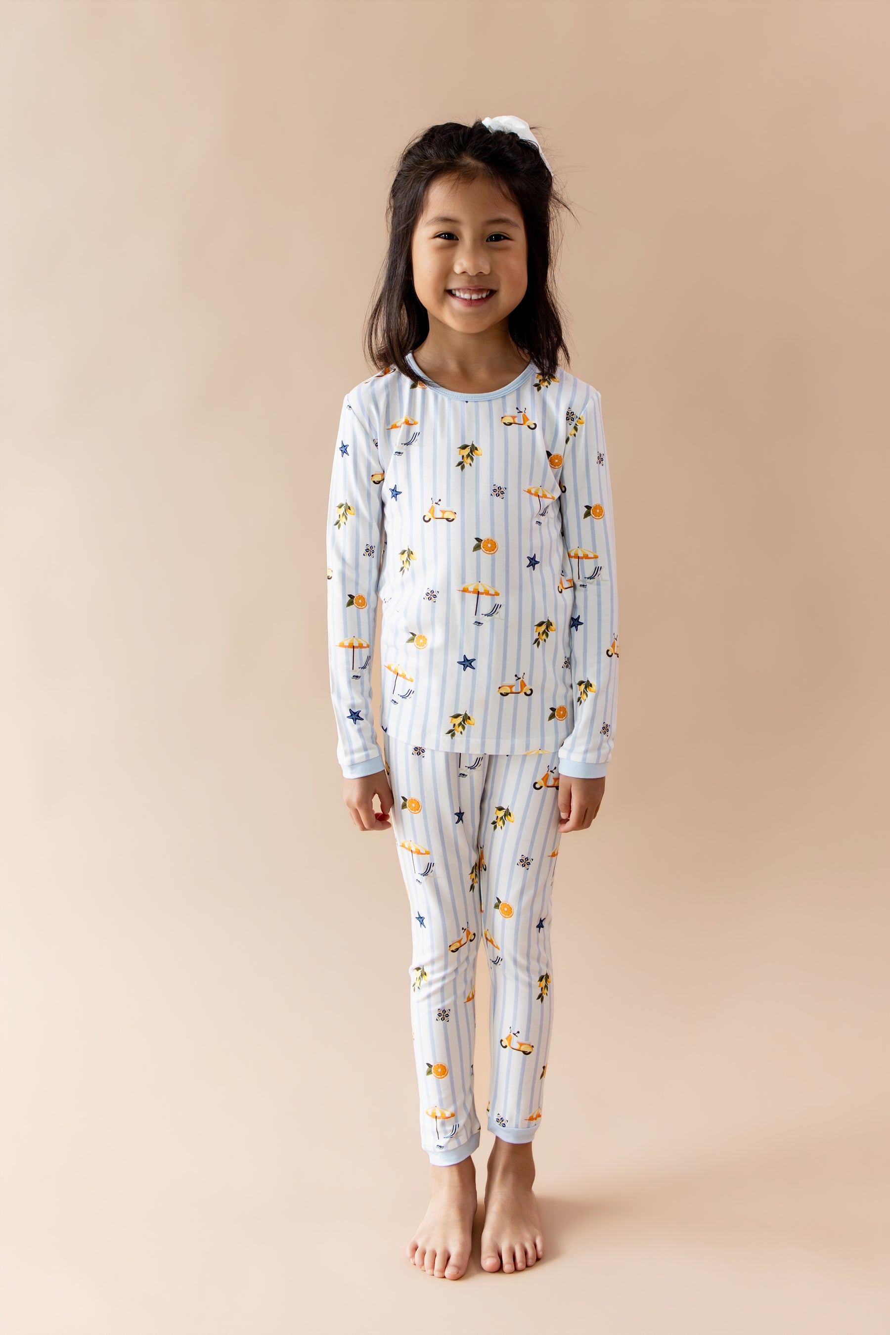 Young smiling girl standing in front of a light beige wearing the Long Sleeve Pajamas in Amalfi Coast