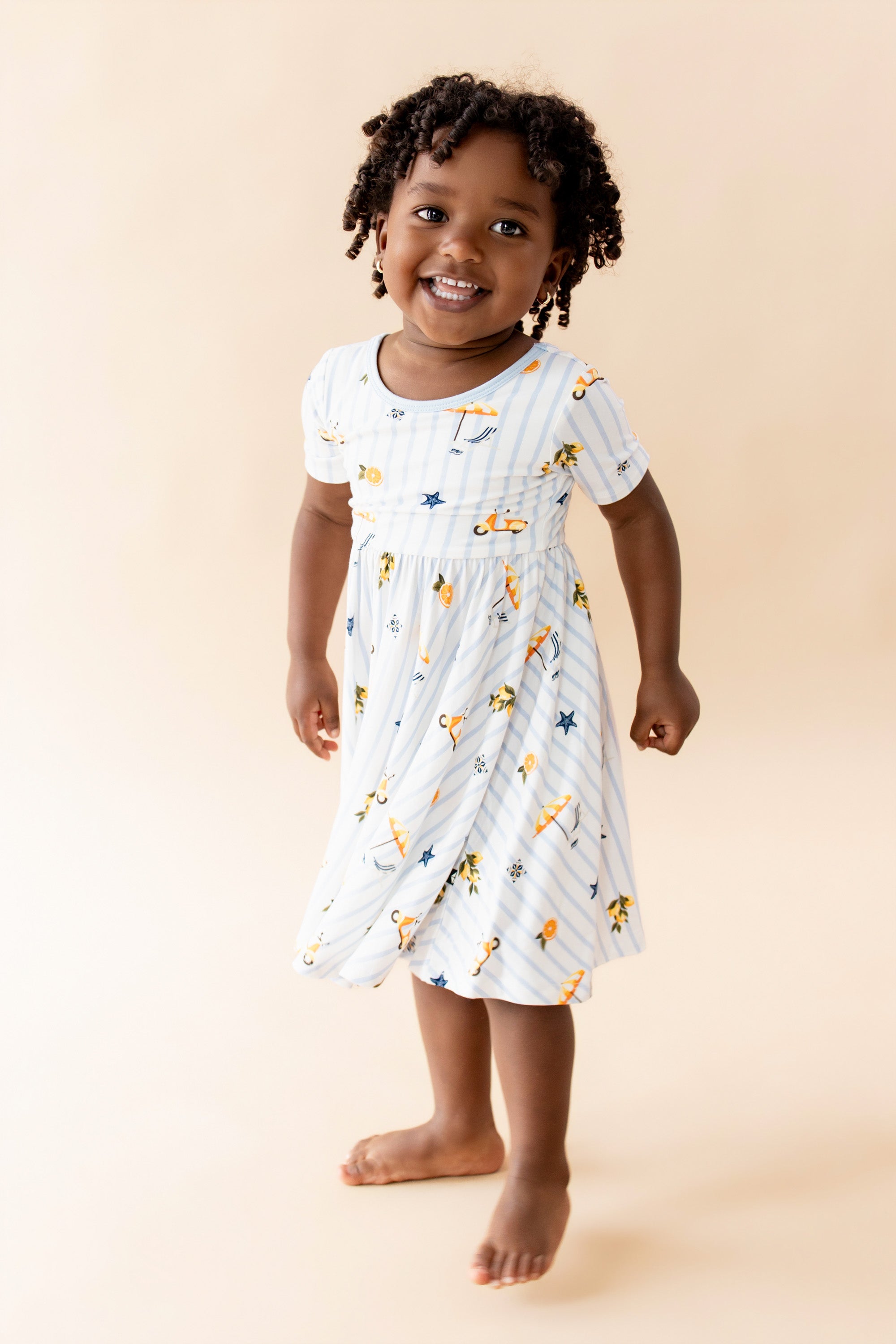 Young girl wearing the Twirl Dress in Amalfi Coast standing in front of a light beige background