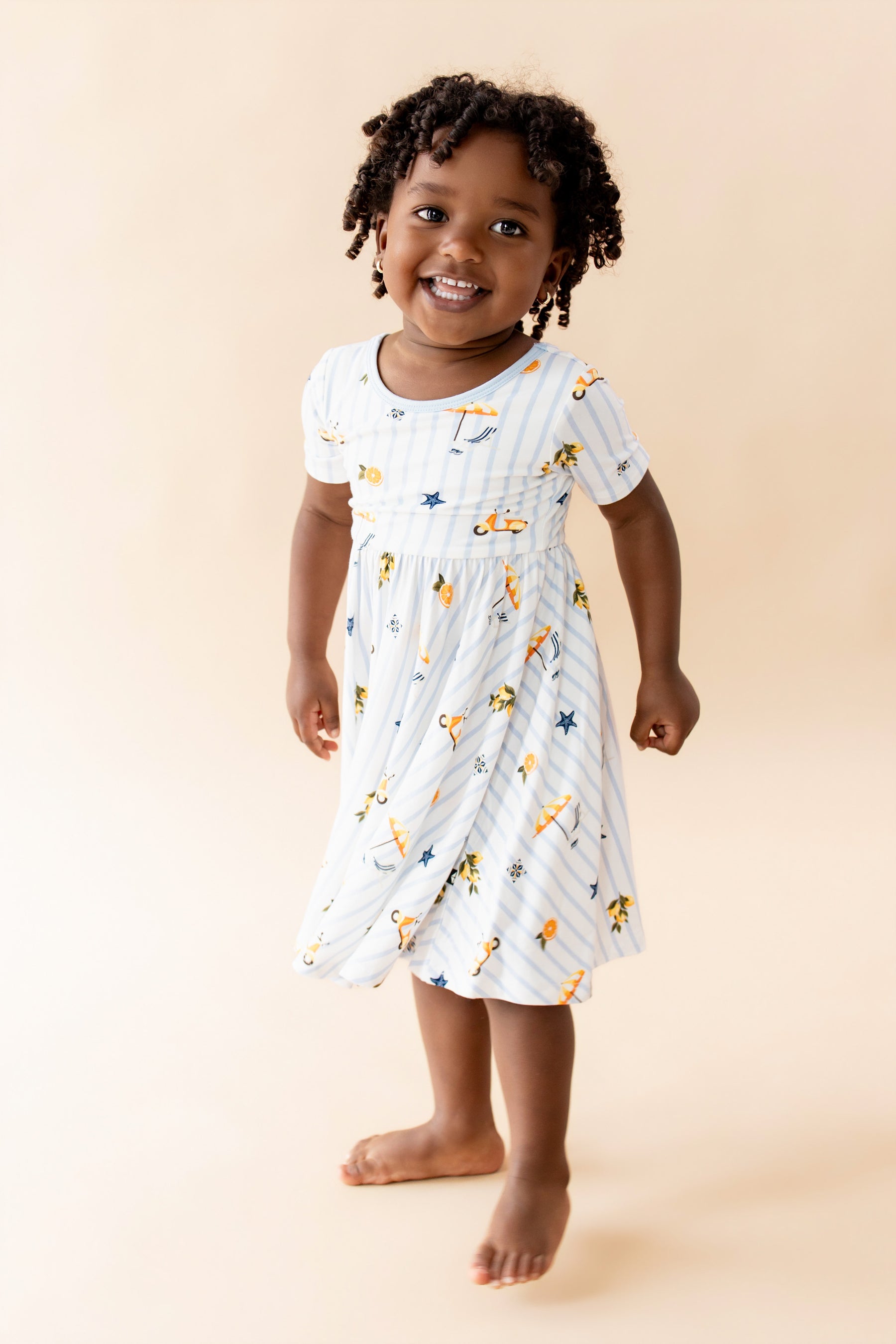 Young girl wearing the Twirl Dress in Amalfi Coast standing in front of a light beige background