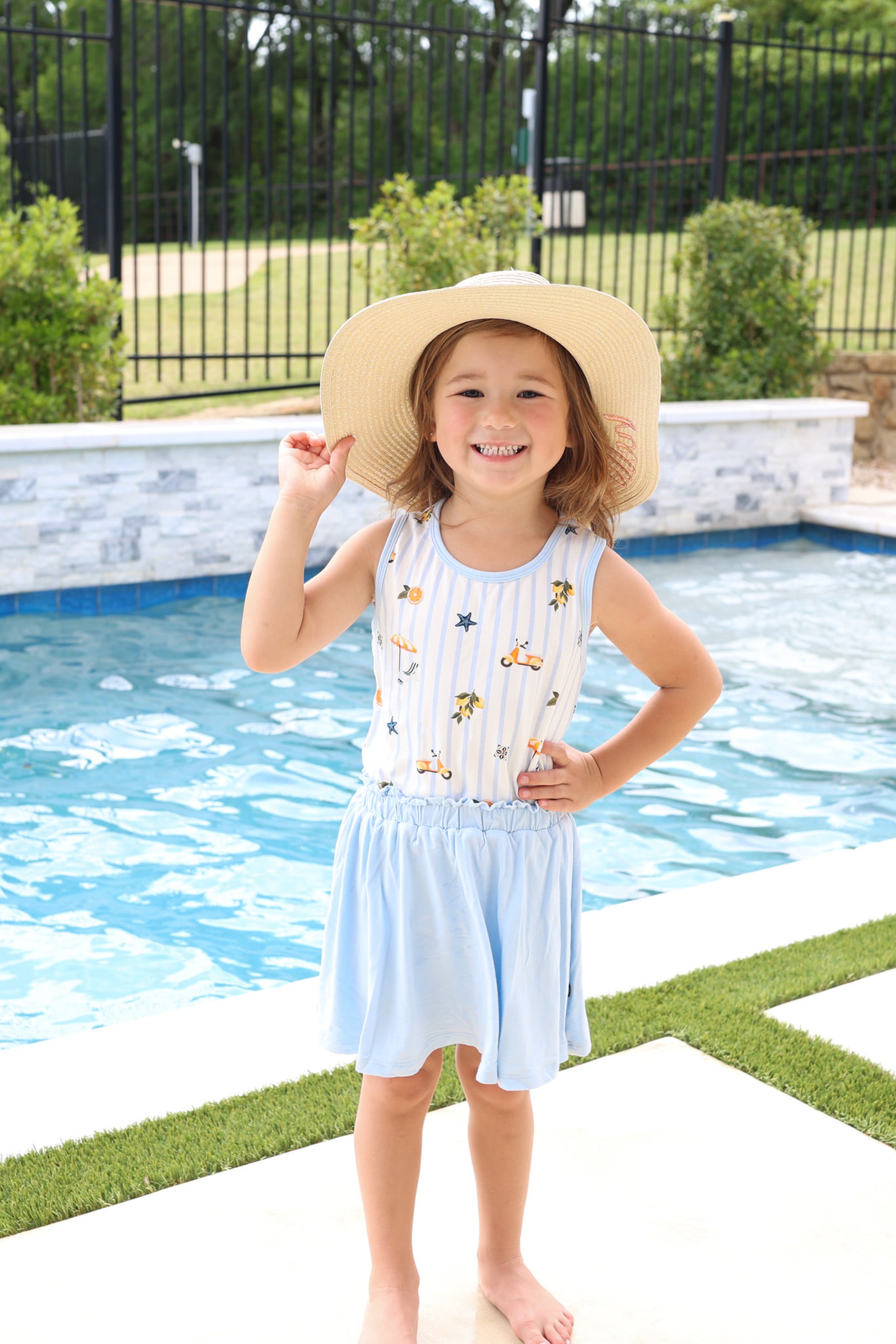 Young girl wearing the Toddler Tank Top in Amalfi Coast with light blue skort and straw hat