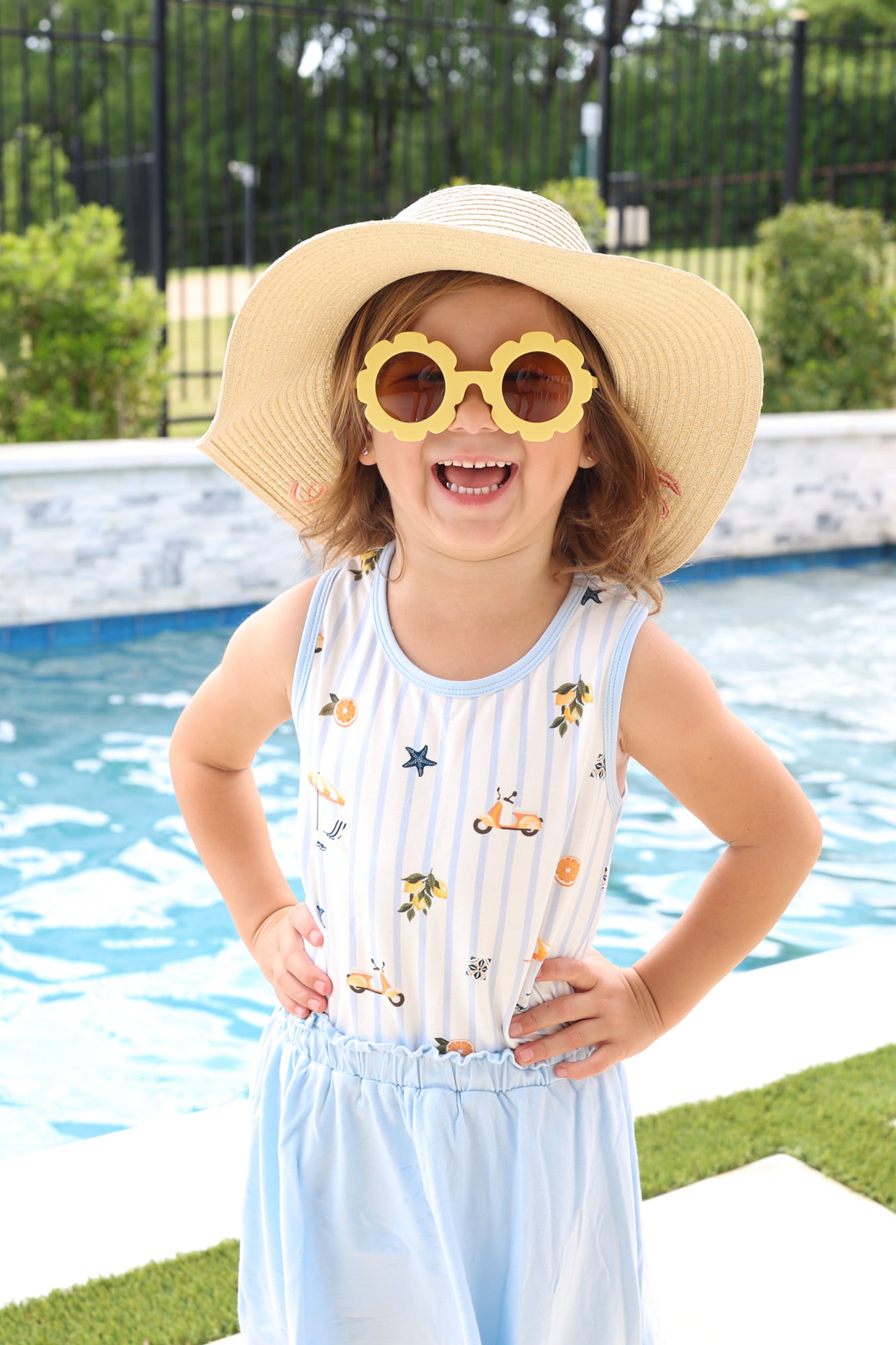 Smiling girl wearing a straw hat and yellow sunglasses wearing the Toddler Tank Top in Amalfi Coast with a light blue skort