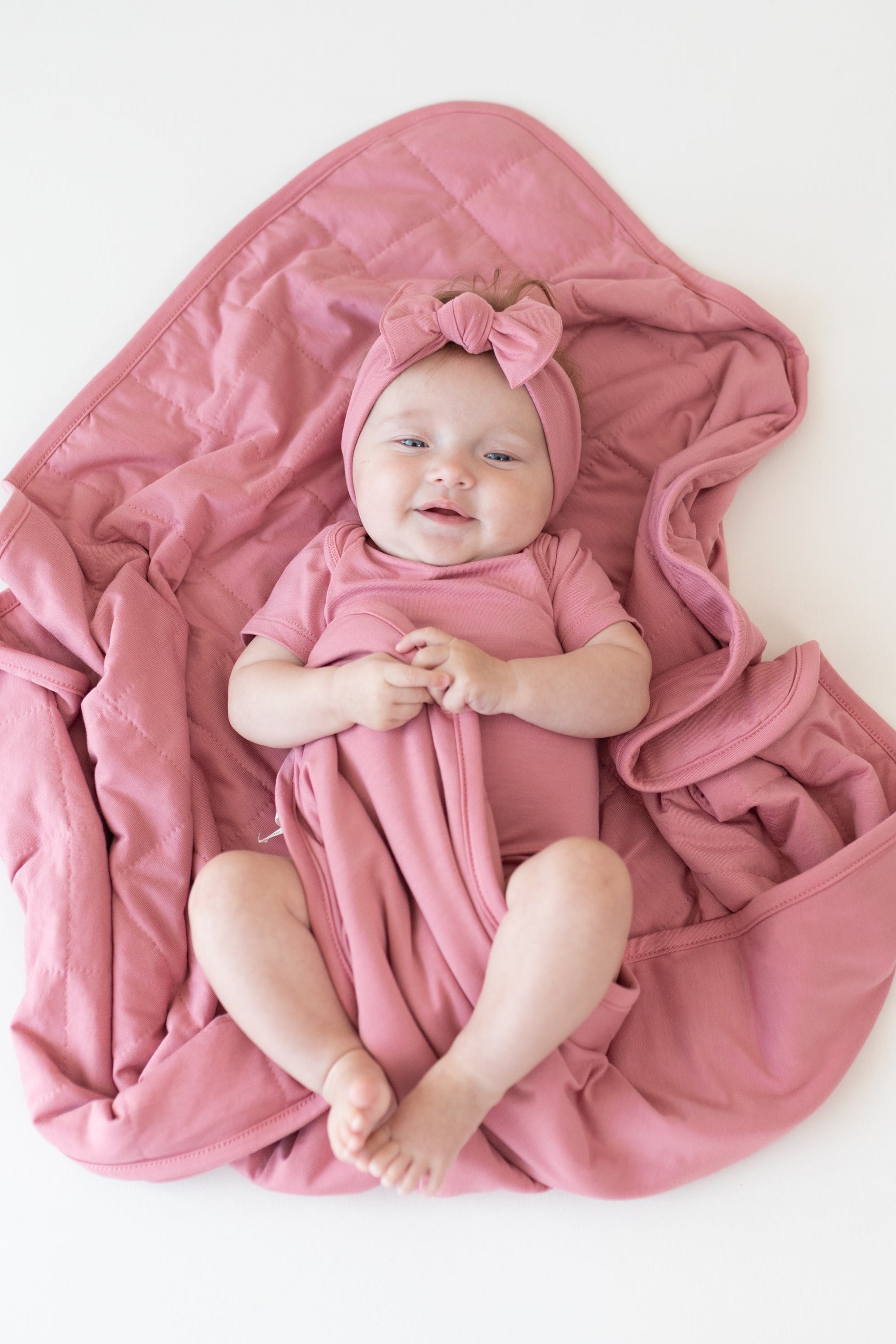 Baby wearing Apple Blossom Bodysuit and Bow laying on matching pink Baby Blanket