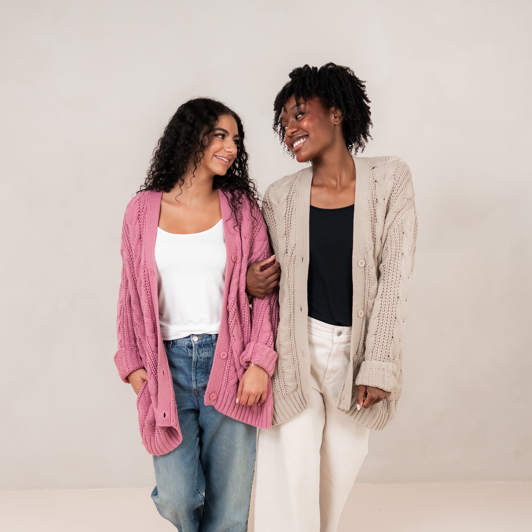 Two models standing side by side wearing the Cable Knit Adult Cardigan in Apple Blossom and Almond