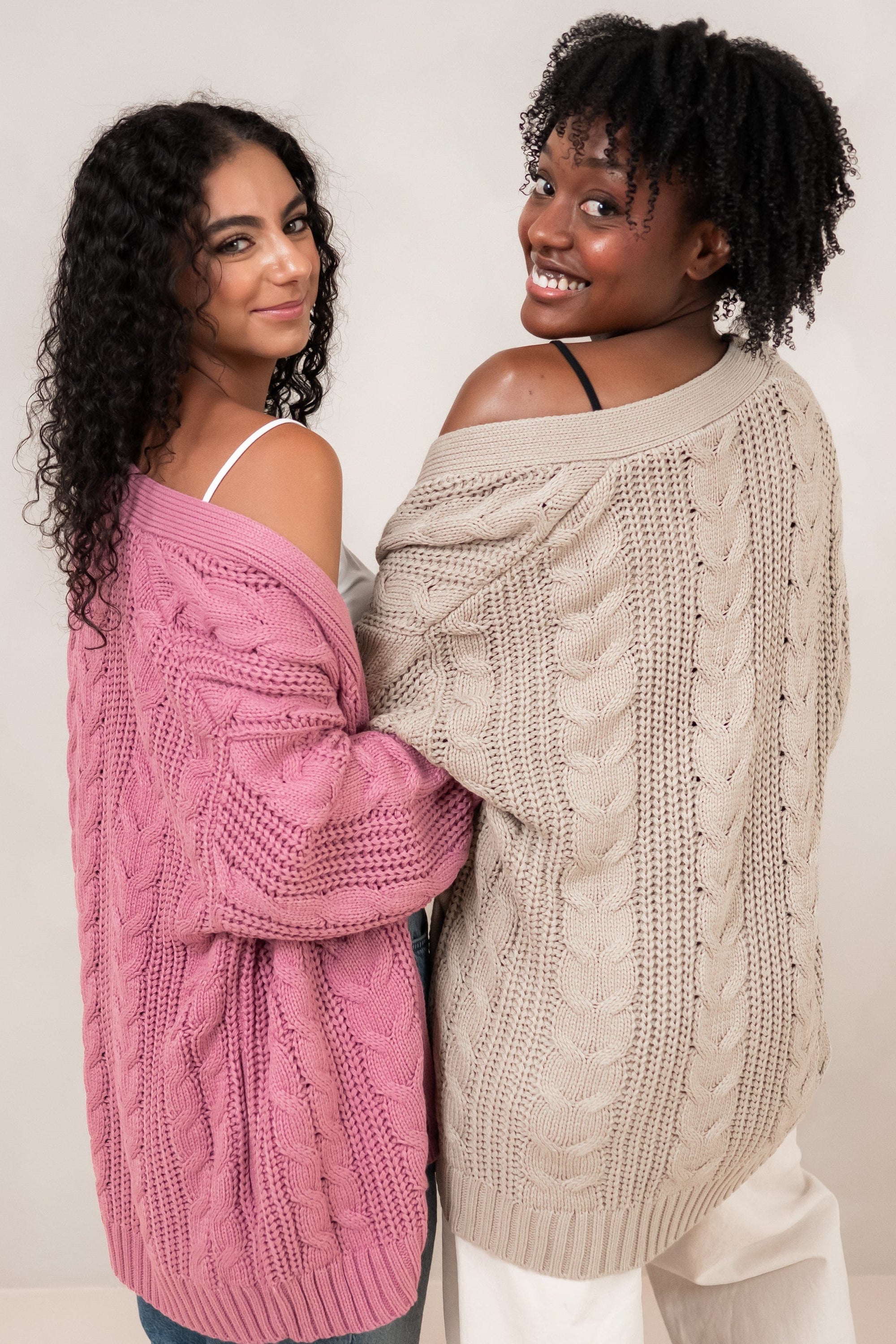 Two models standing side by side with their backs to the camera wearing the Cable Knit Adult Cardigan in Almond and Apple Blossom
