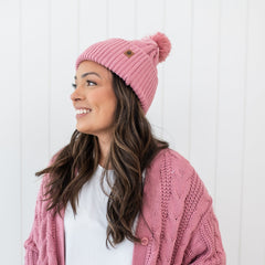 Smiling female model wearing the Cable Knit Adult Pom Beanie in Apple Blossom with matching cable knit cardigan